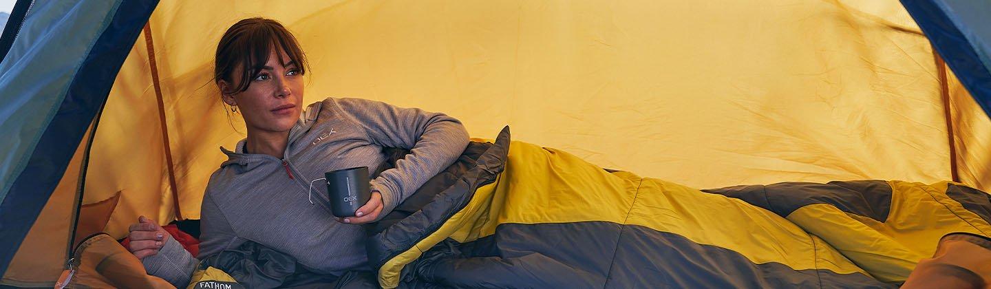 Person lay down in a sleeping bag inside of a tent
