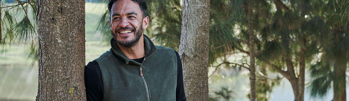 Person wearing a gilet leaning up against a tree