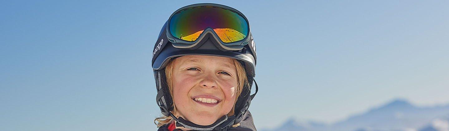 A closeup of a child wearing ski goggles and a helmet