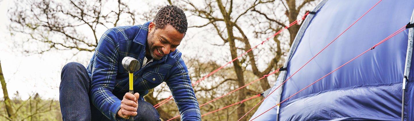 A person hammering in tent pegs with a mallet