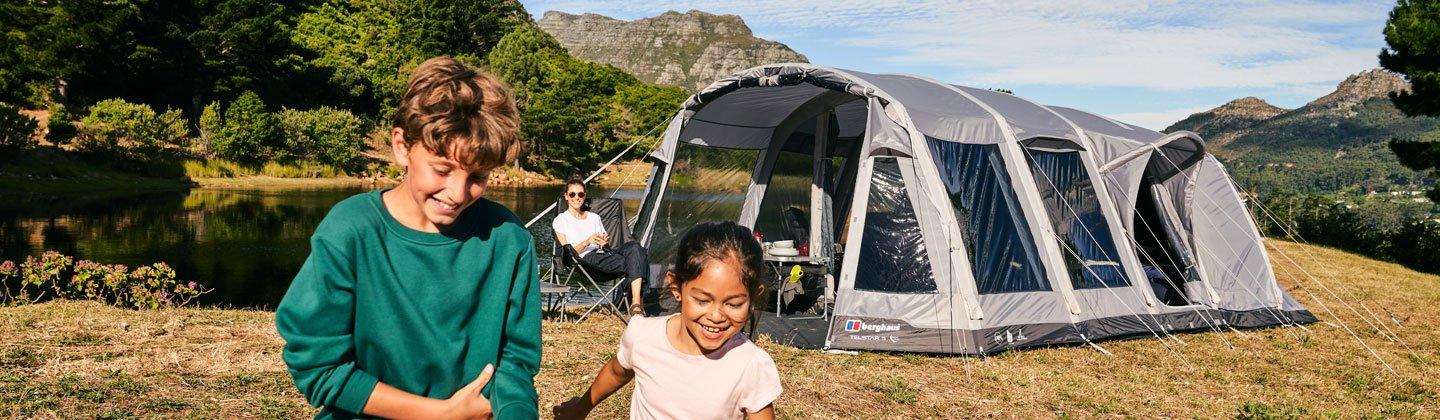 Kids playing in a field with their parents relaxing at the tent in the background