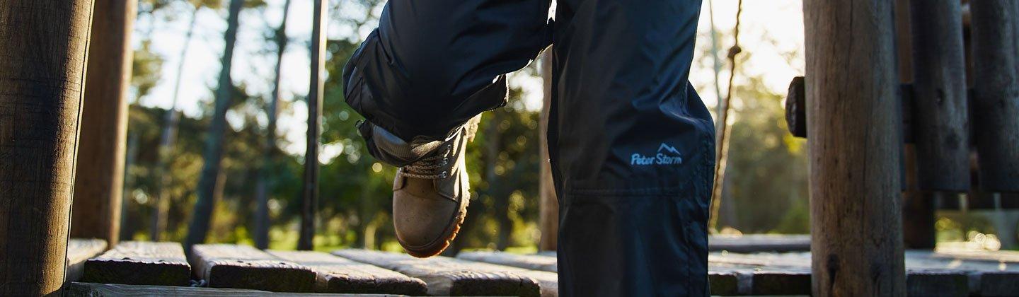 Closeup of a child wearing waterproof pants walking along a wooden bridge