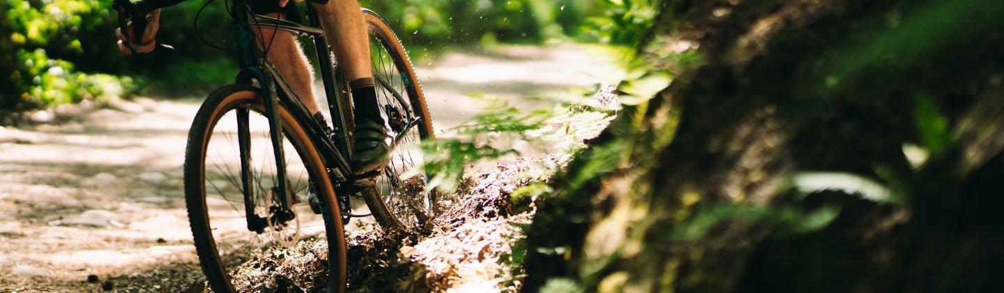 Closeup photo of a person cycling through a forest with the focus on the wheels and tyres