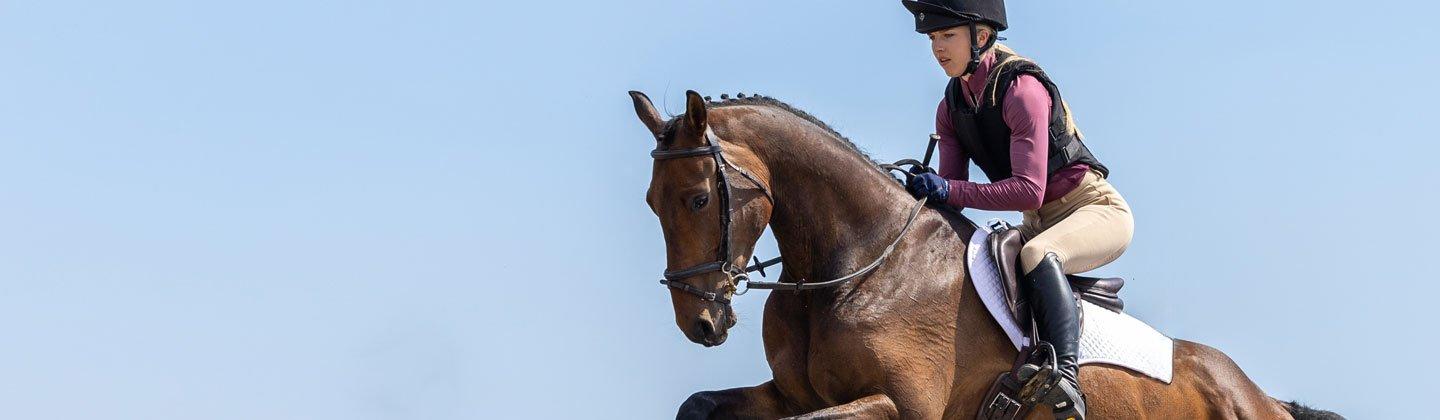 A person riding a horse over a jump wearing a body protector