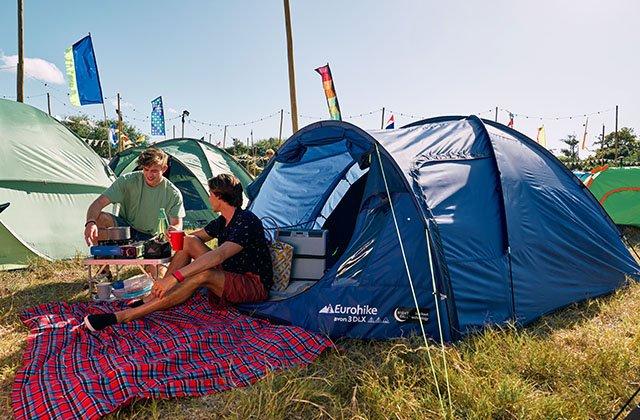festival goers sitting in a field on a blanket next to a tent