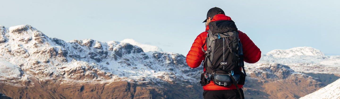 A person wearing a small day pack walking with snow-capped mountains in the distance