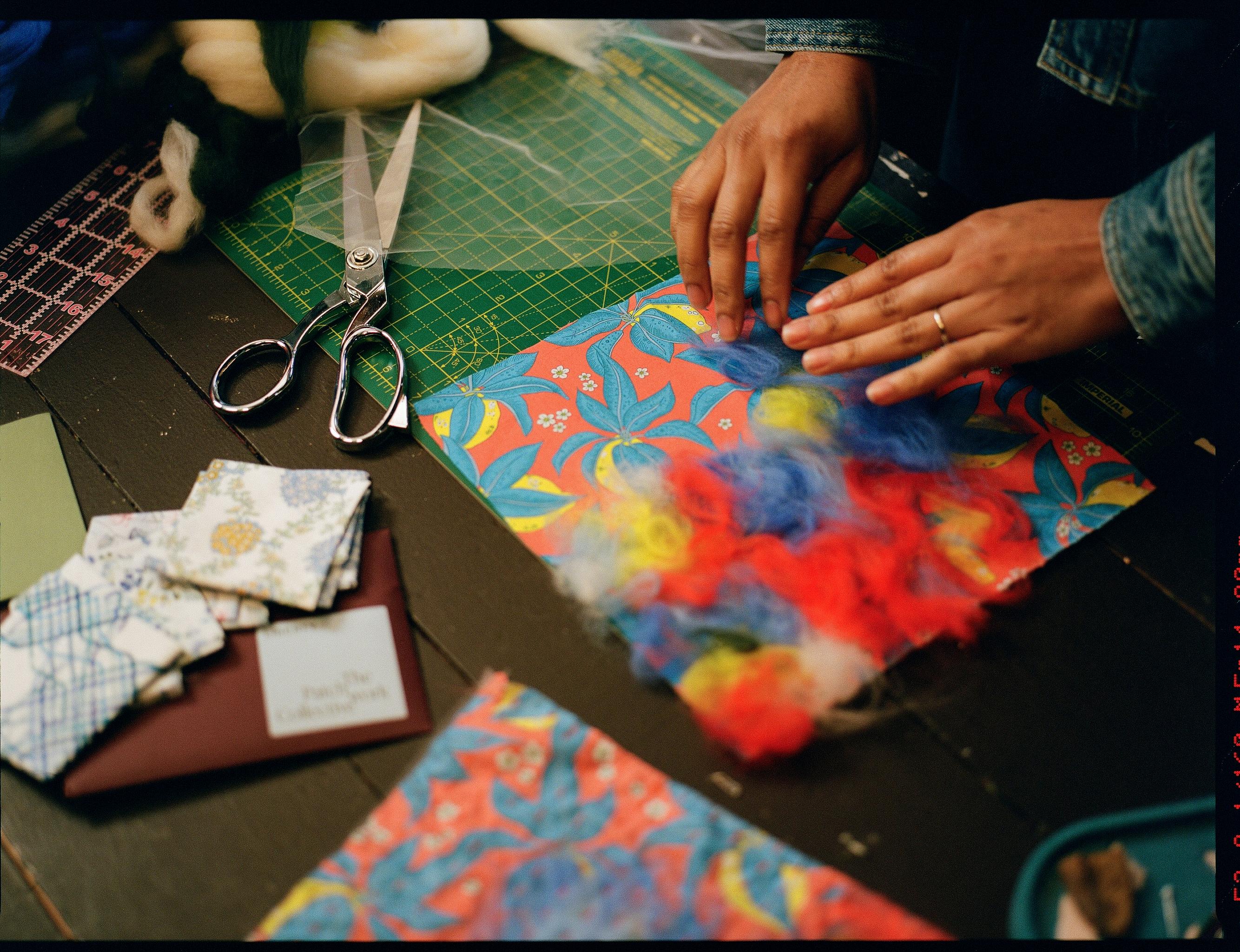 A multicoloured square of Liberty fabric lies on a table, being worked on by a pair of hands