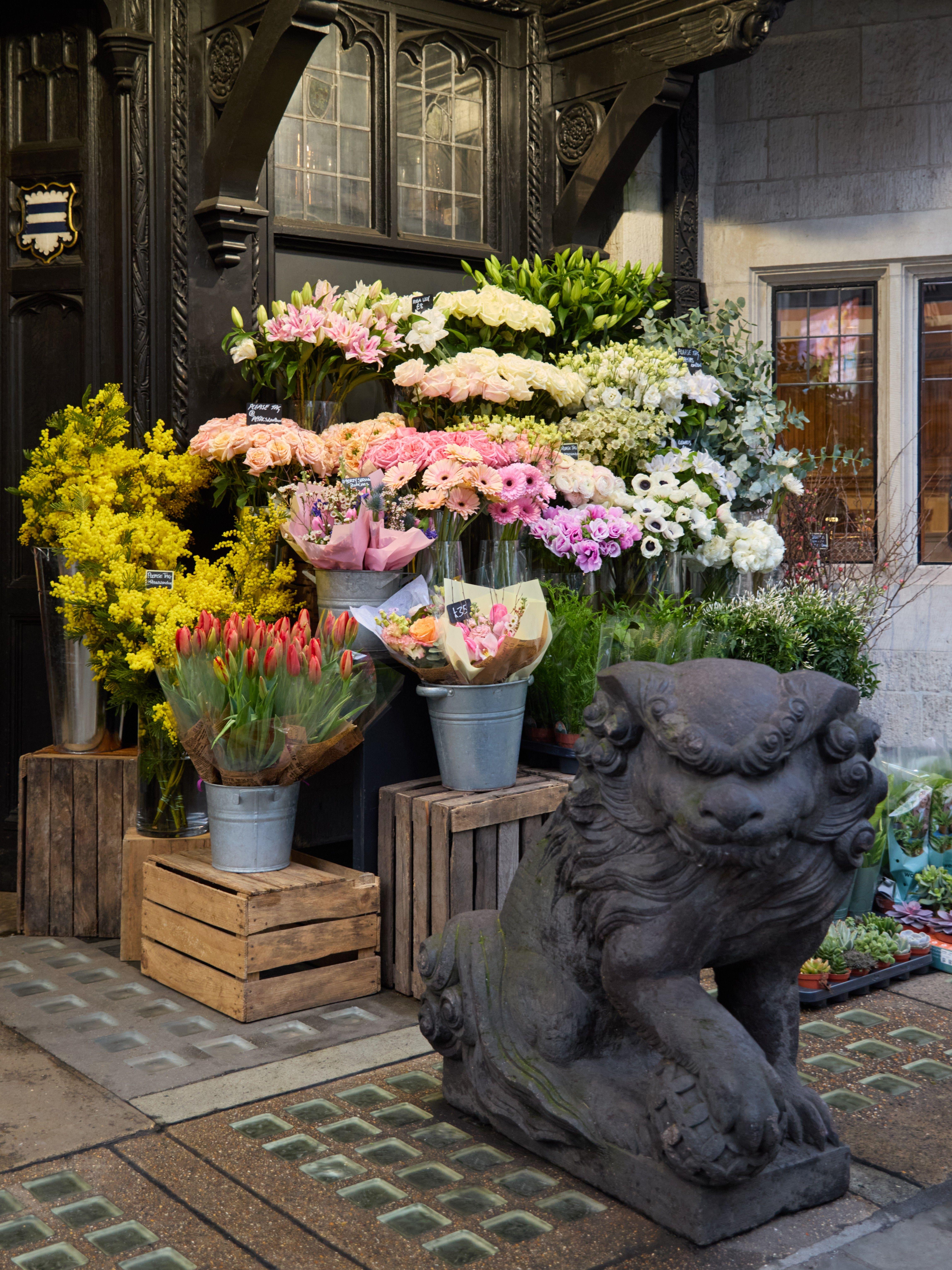 A display of colourful flowers and bouquets is arranged outside Liberty London, behind an ornamental lion at the store's front door