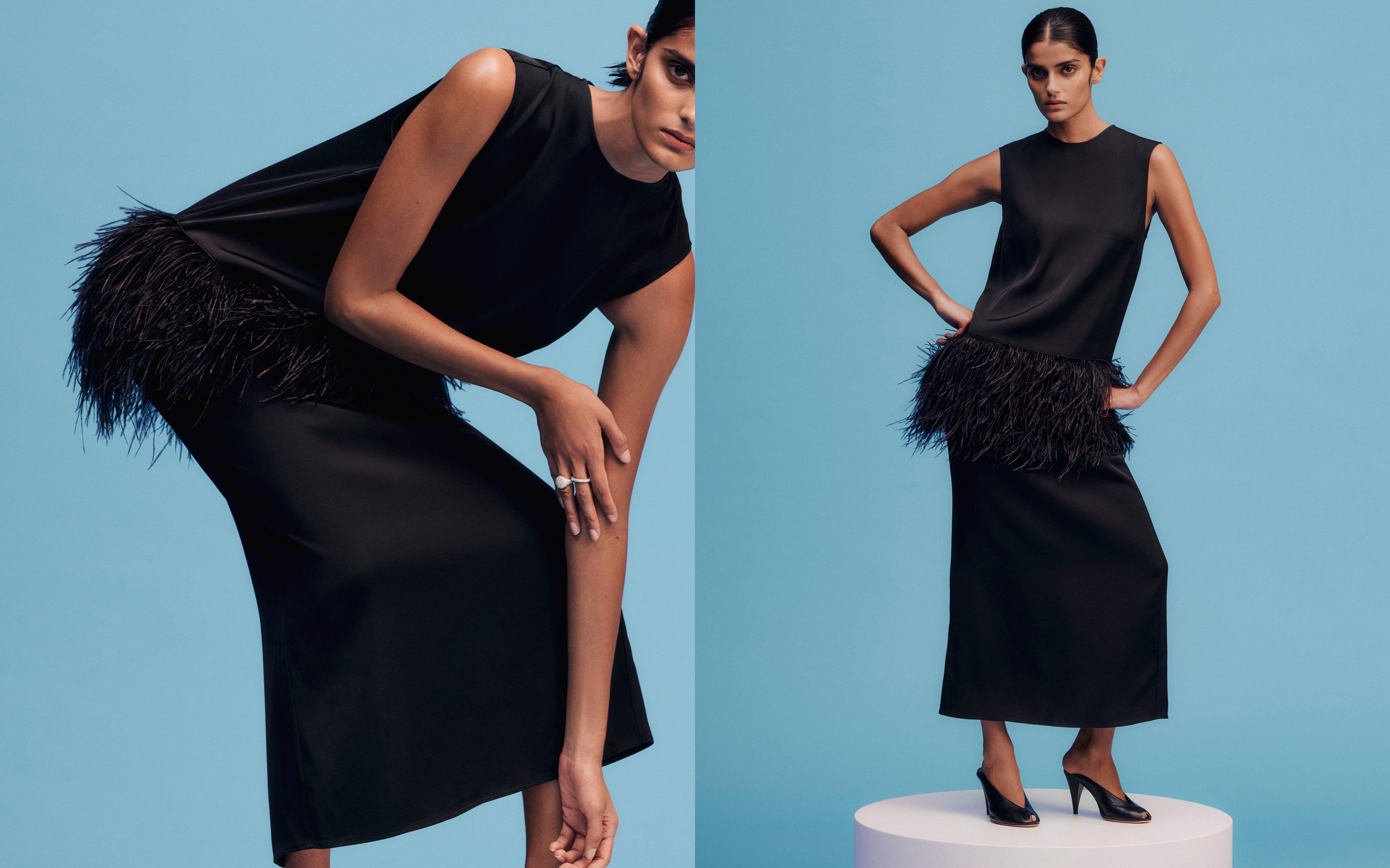 Model wears a black dress with feathered trims, and black mules 