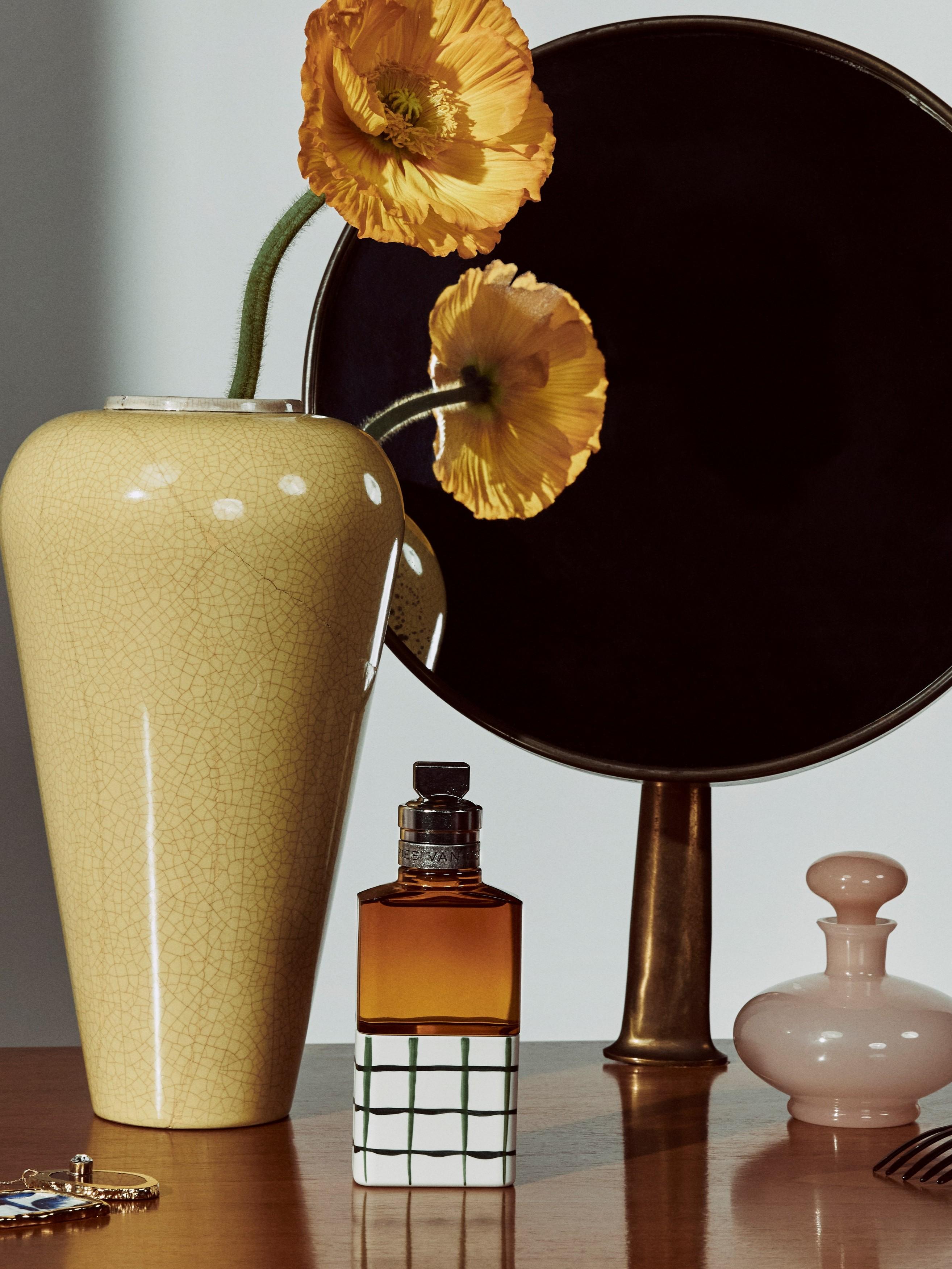 Dries Van Noten fragrance bottle on a vanity, next to a vase containing yellow-gold poppies 