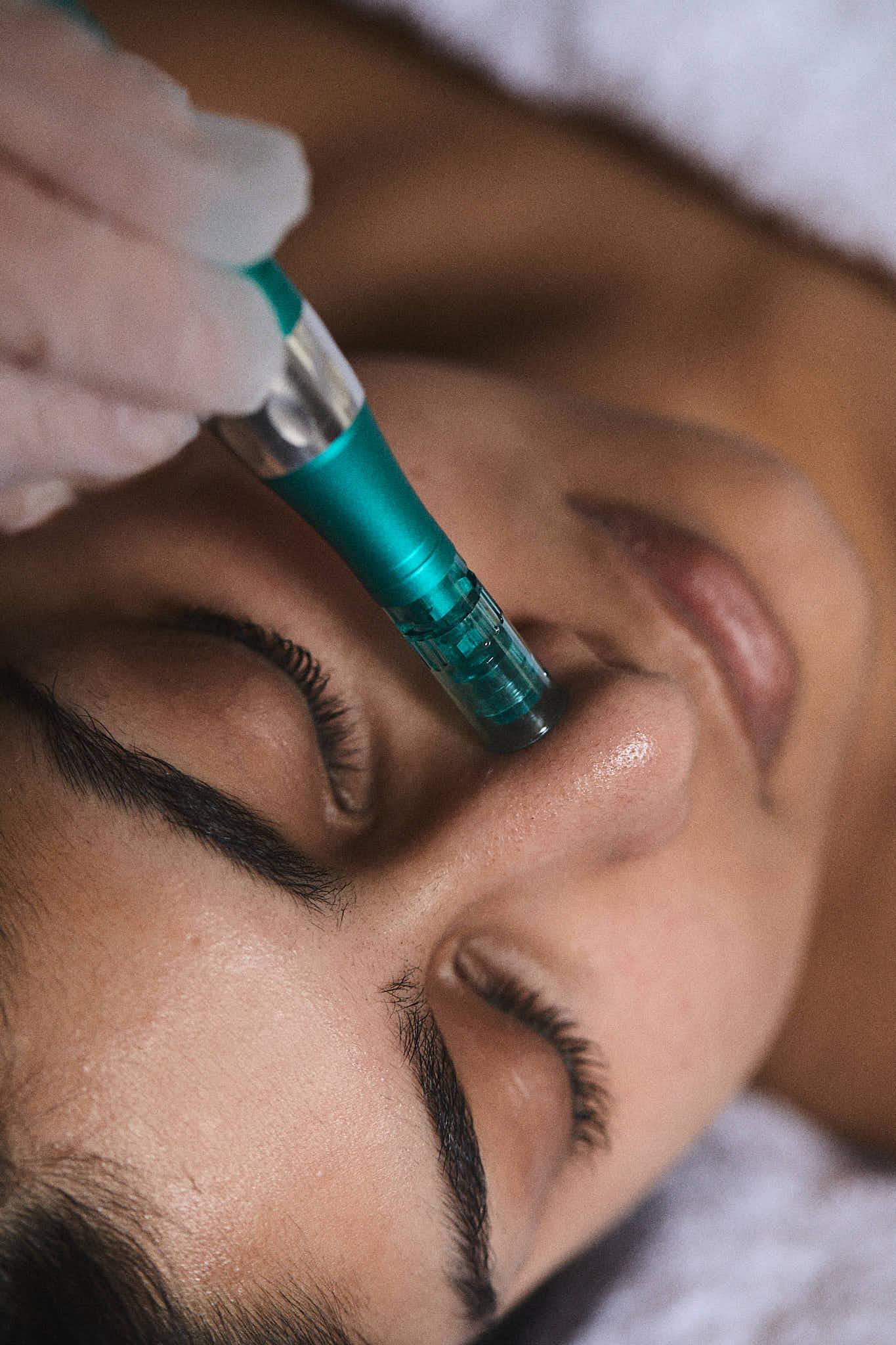 A woman's face appears with a turquoise device adminstering a skincare service