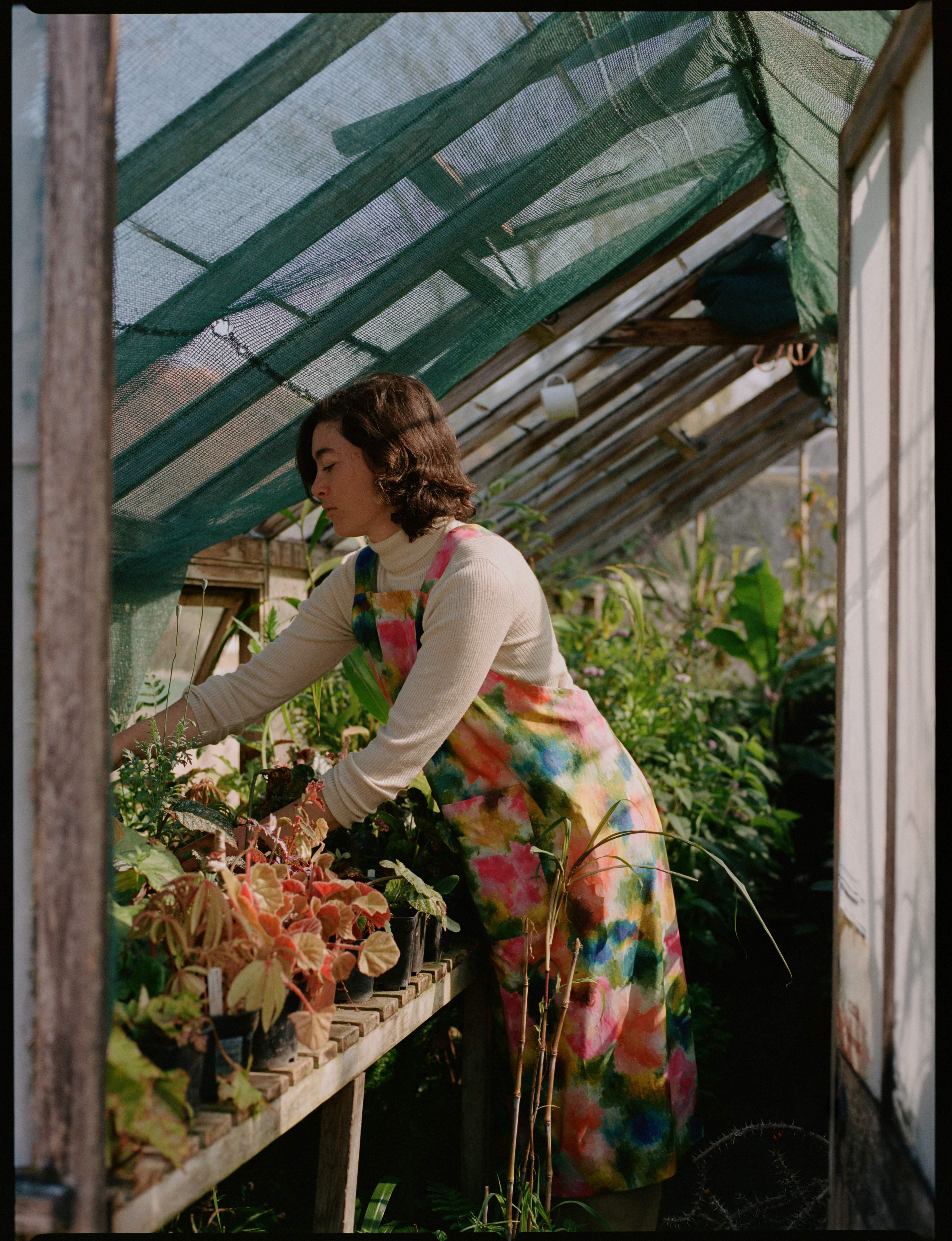 Model wearing Liberty Fabrics AW26 collection tends to plants in a greenhouse