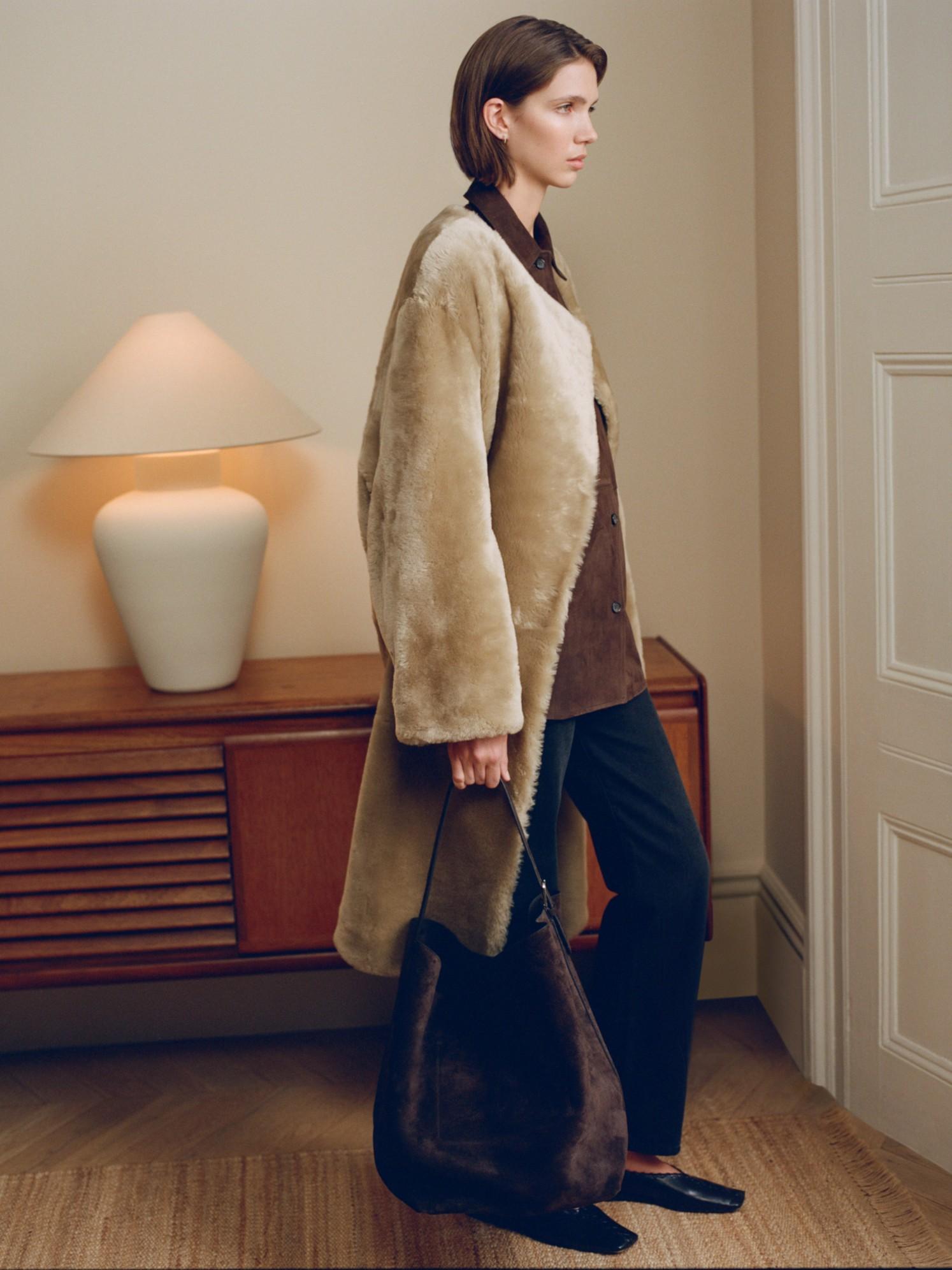 Model wears a TOTEME coat, knit, trousers and bag