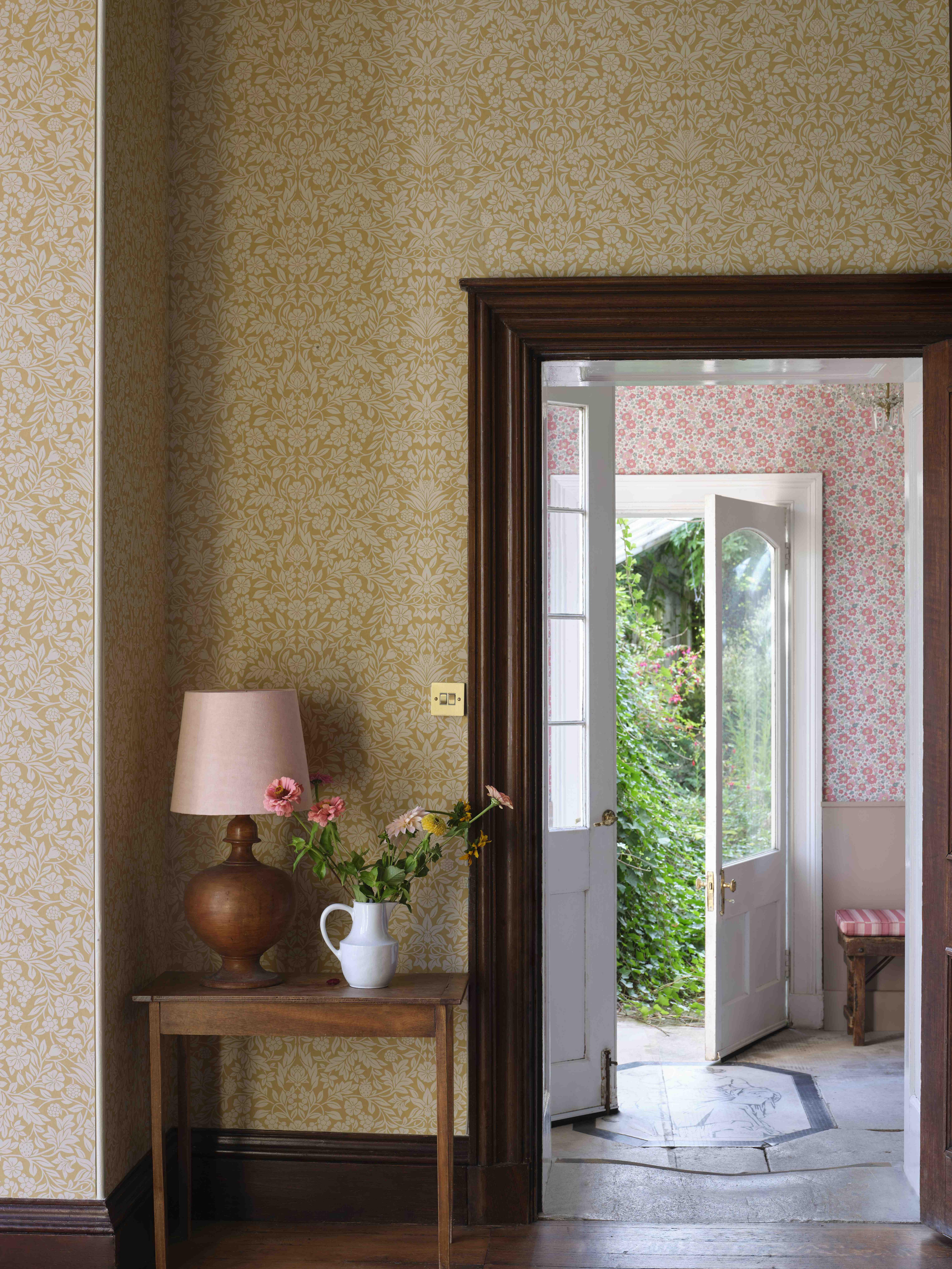 A doorway adorned with Liberty London wallpapers and opening into a bright, green garden