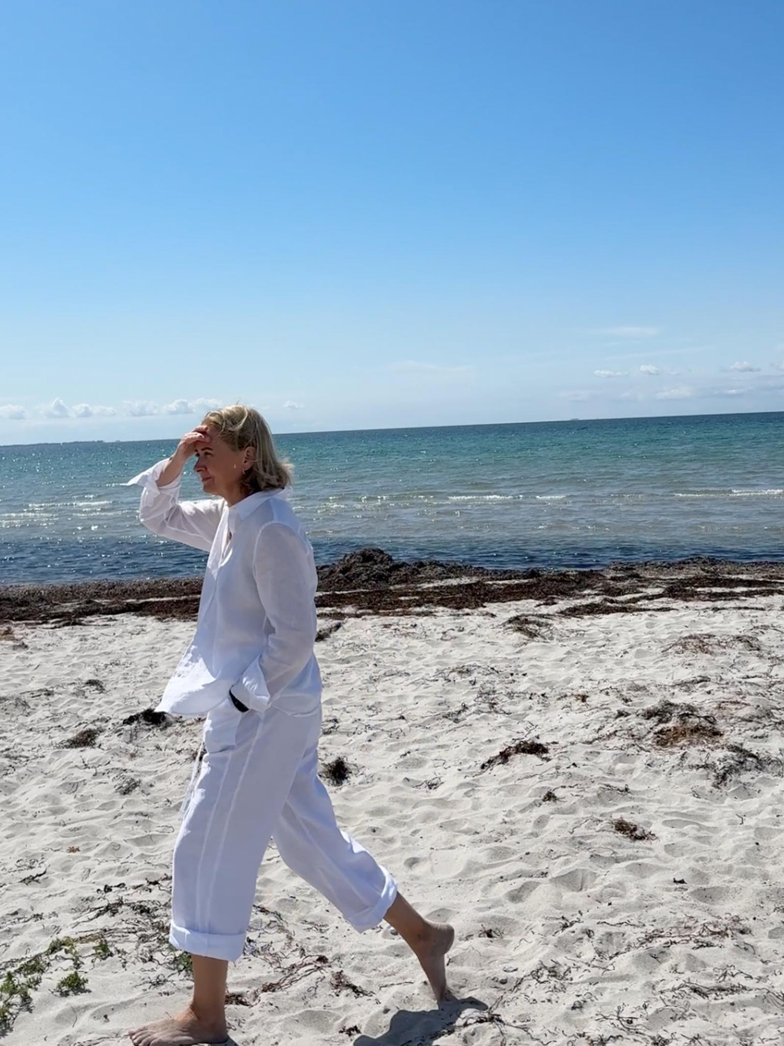 A woman walking on a pristine white beach, wearing an all white linen outfit