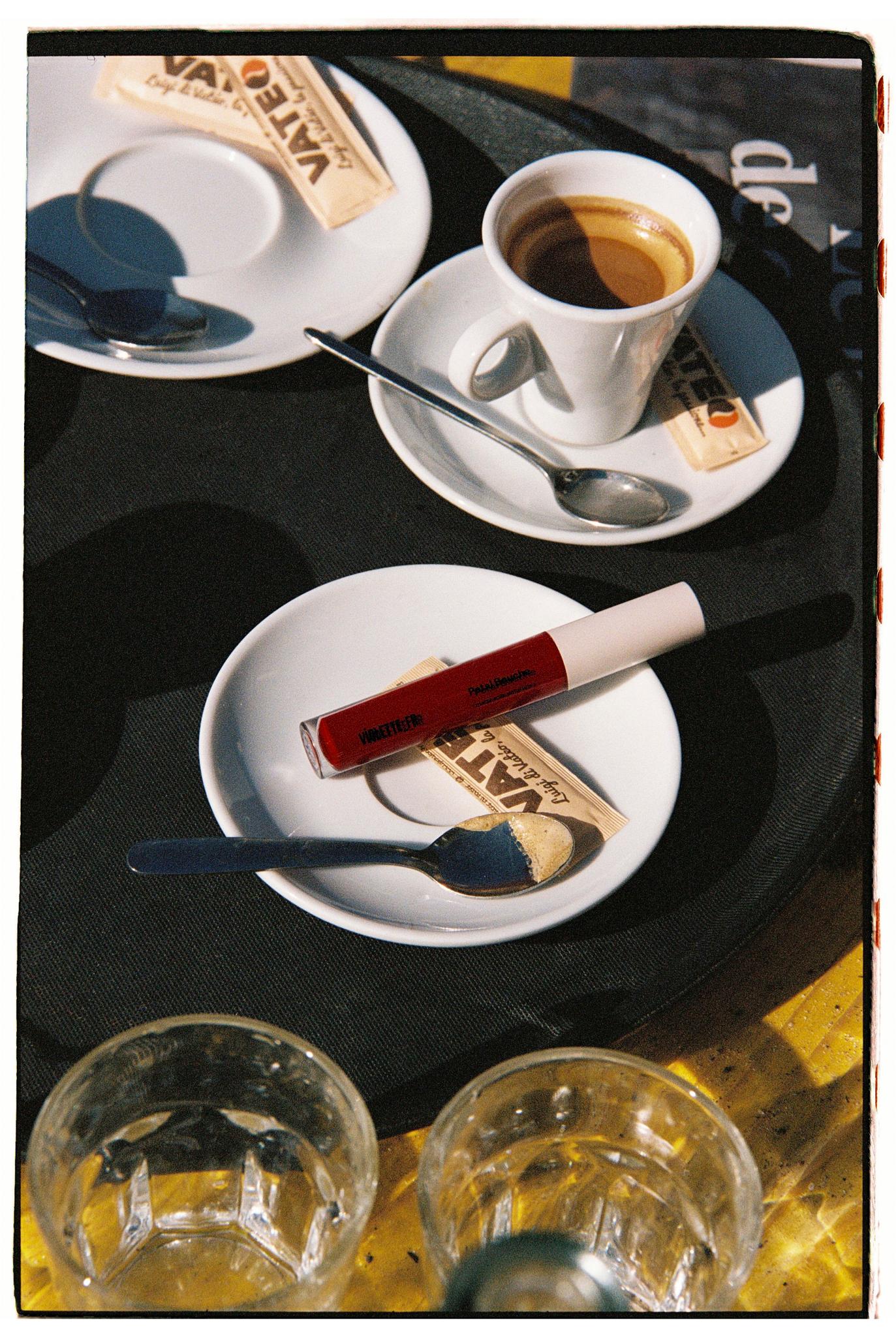 A cafe table is set with coffee cups, water glasses and lipstick