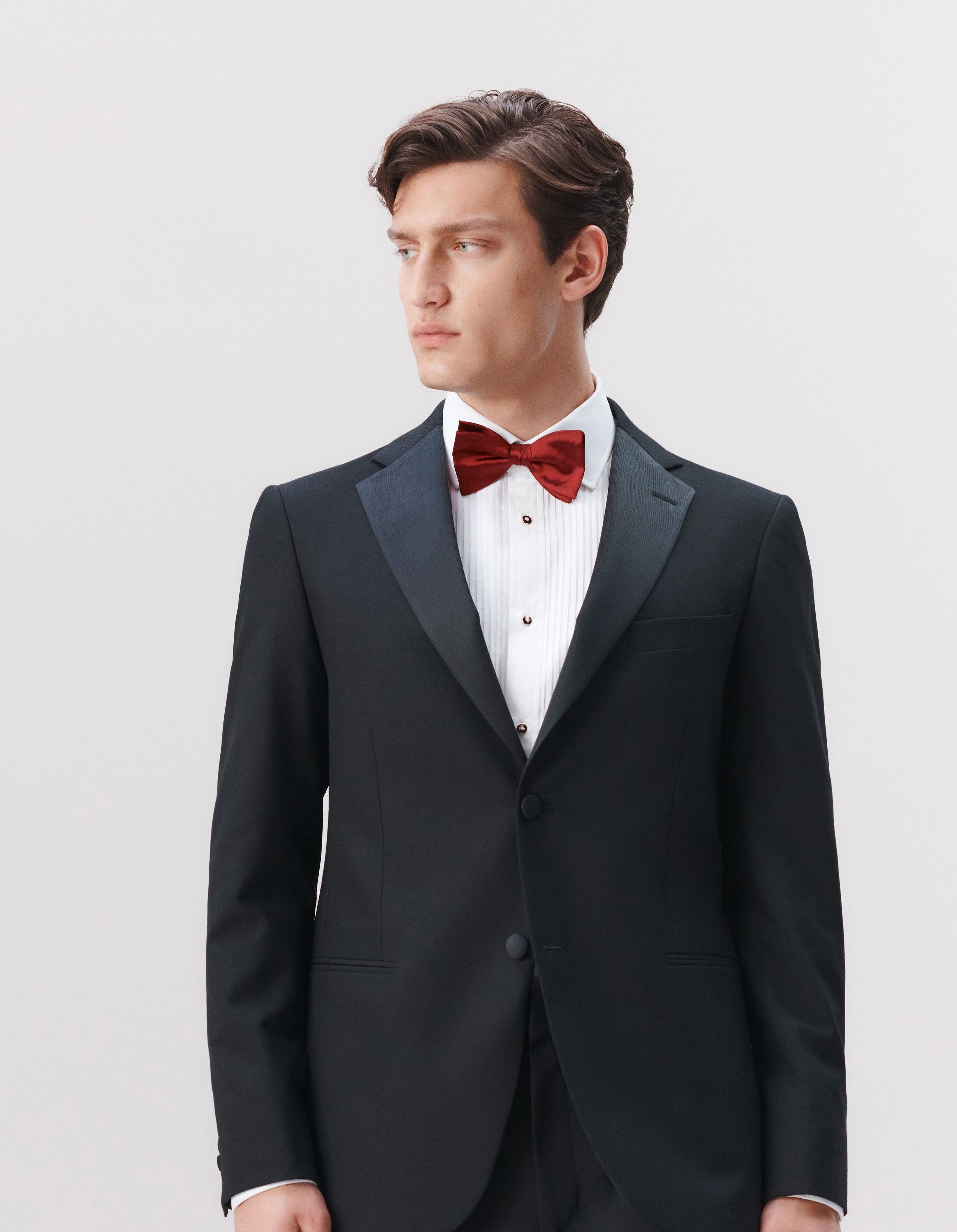 A man wears a black evening jacket, white evening shirt with a red bow tie