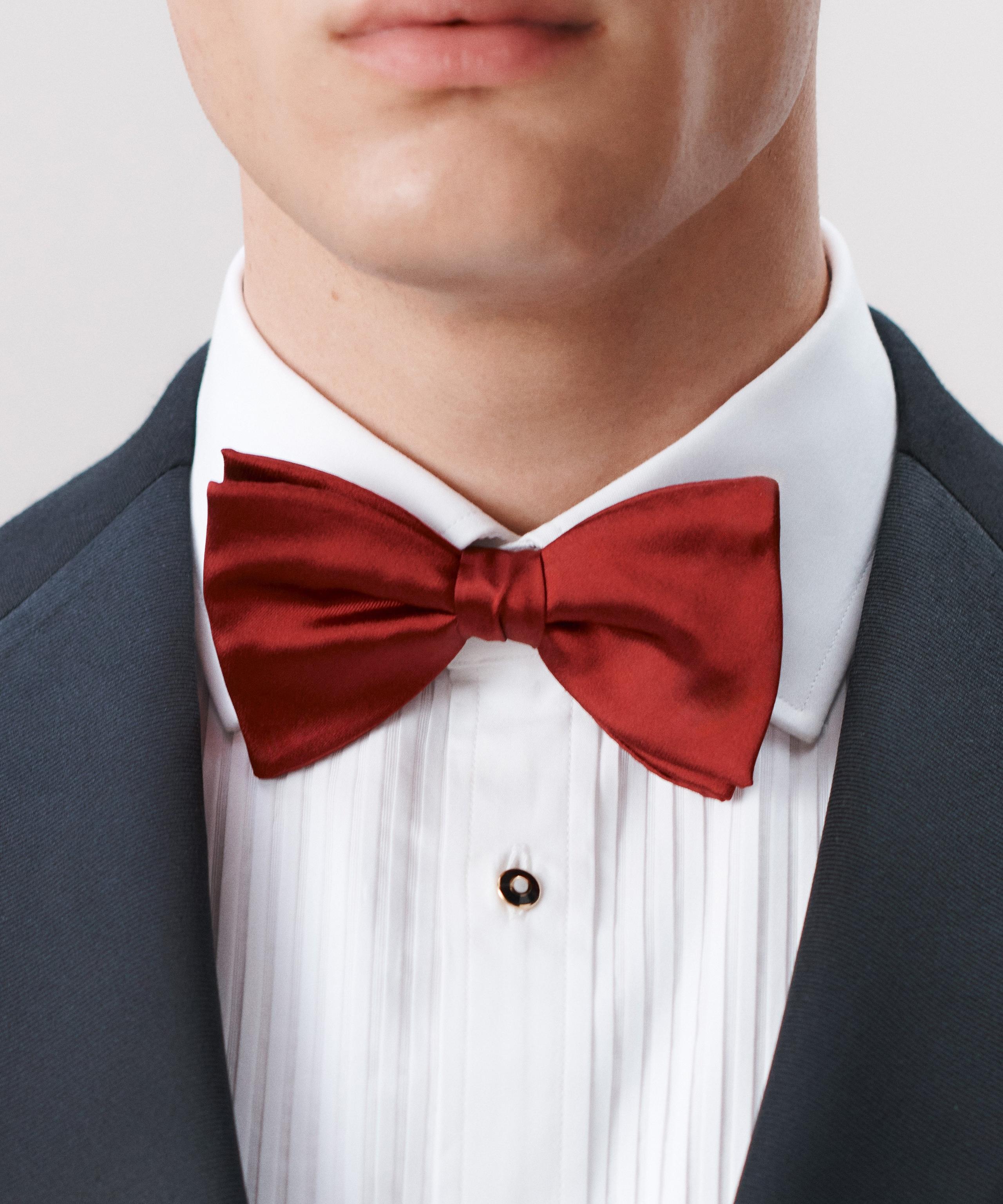 A close up of a man wearing a black evening jacket, white evening shirt with a red bow tie
