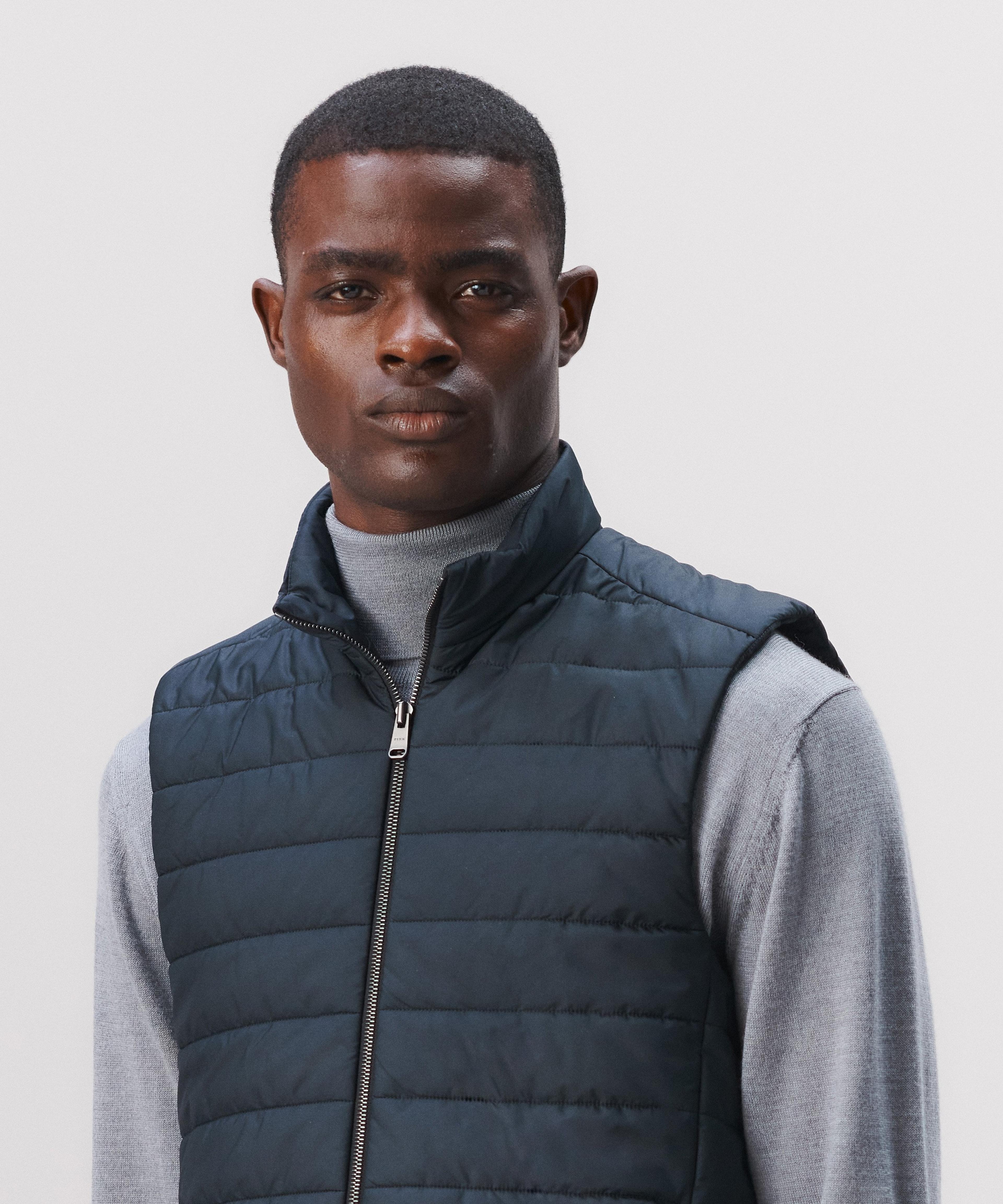A man wears a grey roll neck sweater with a navy padded gilet