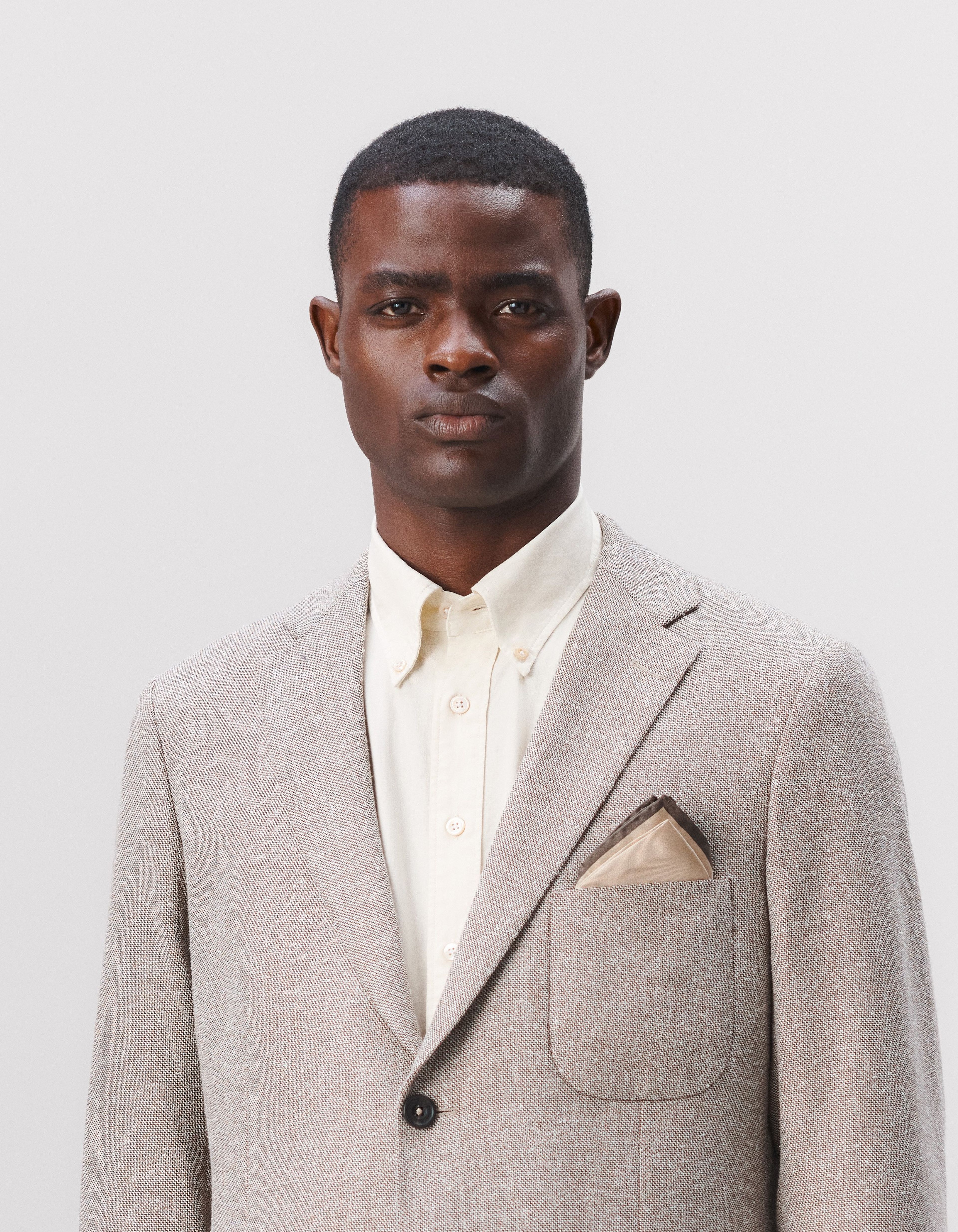 A man wearing a button down collar shirt with a beige suit jacket, styled with pocket squares
