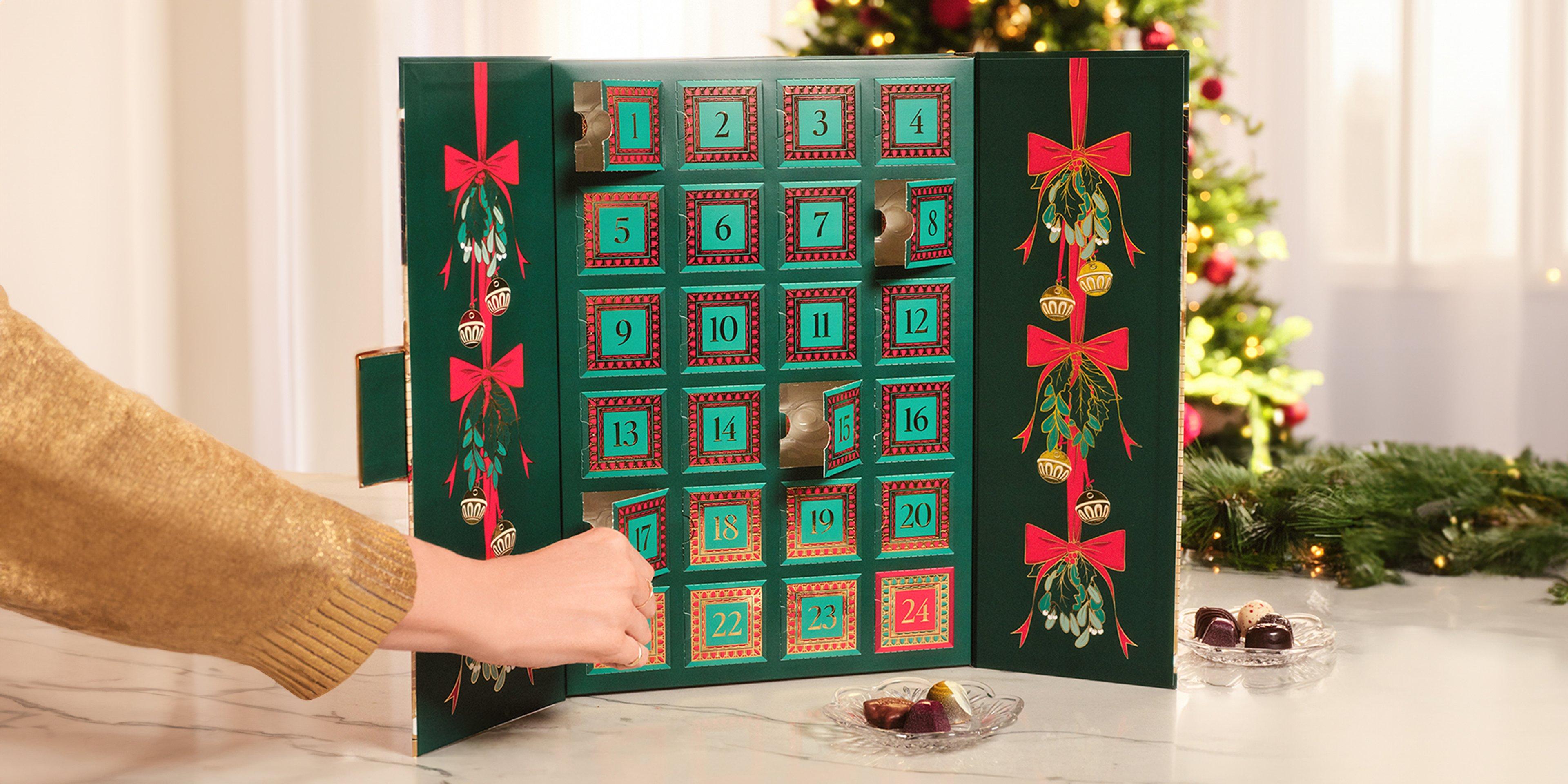 Advent Calendar on table and hand opening door with chocolate gem inside