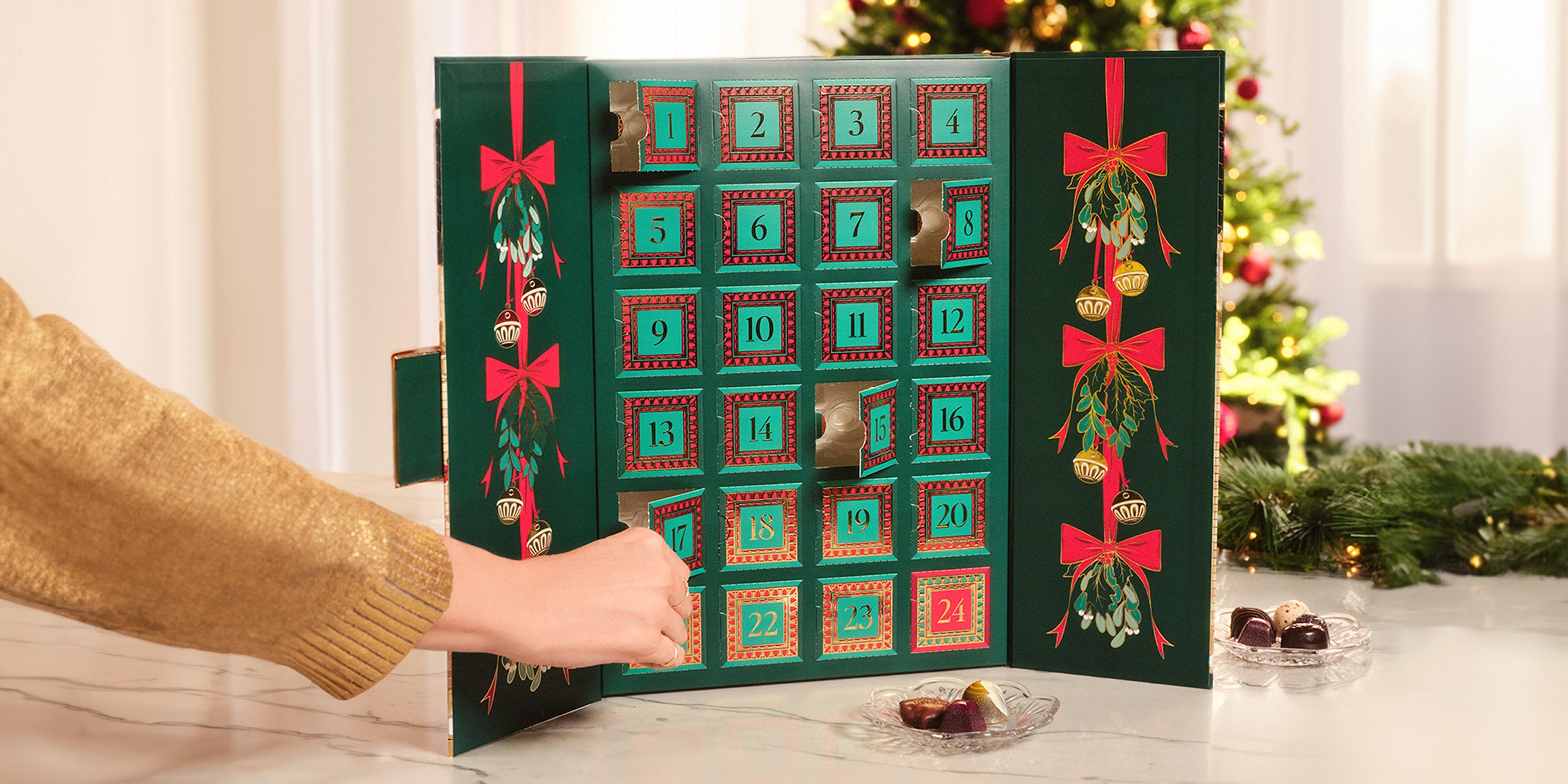 Advent Calendar on table and hand opening door with chocolate gem inside
