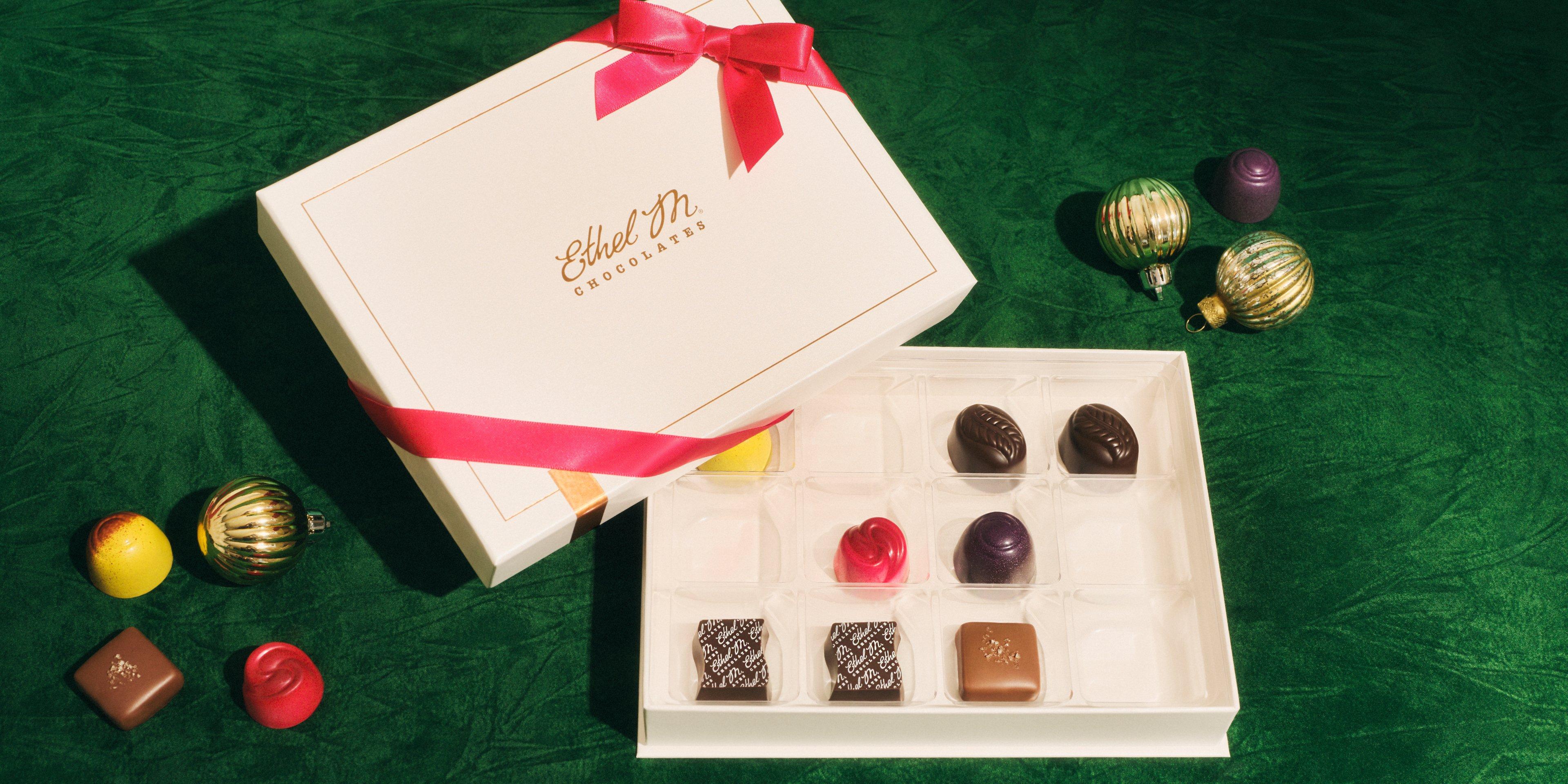 12 piece Cream Custom Chocolate Box with Red Ribbon filled with an assortment with gems and ornaments on green background