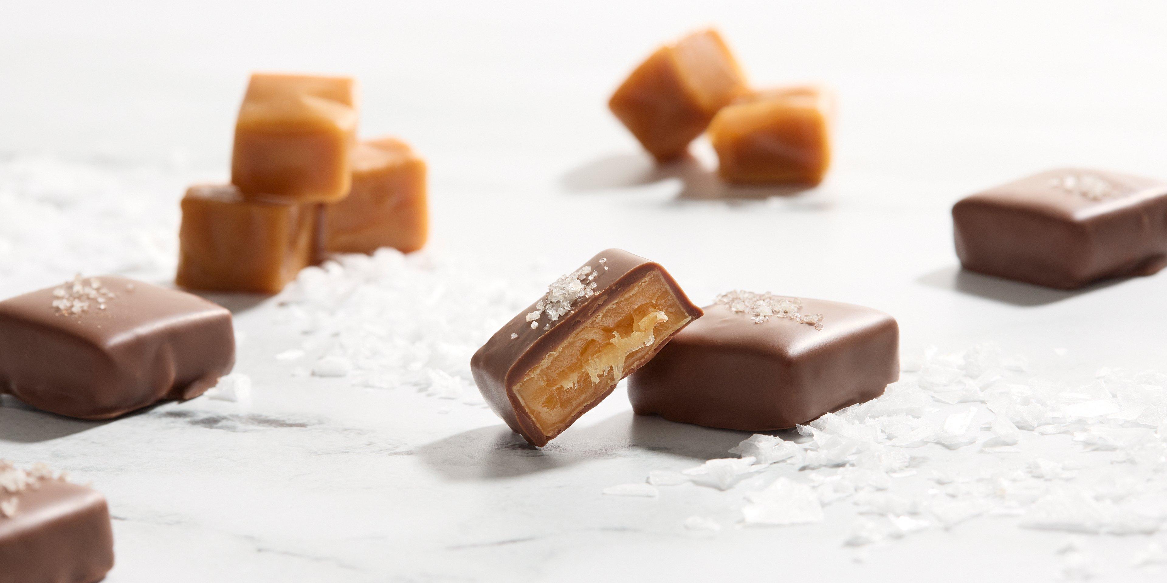 Sea Salt Caramel Milk Chocolate opened on marble background with caramel blocks and salt