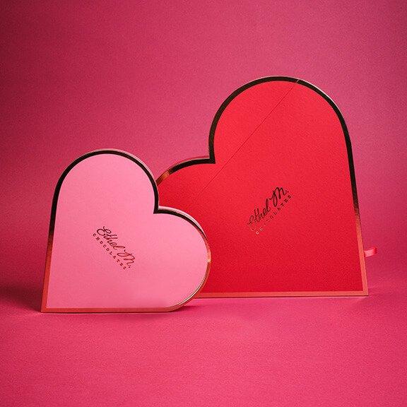 A man handing a woman an Ethel M Chocolates a cream colored Custom Chocolate Box with a red ribbon