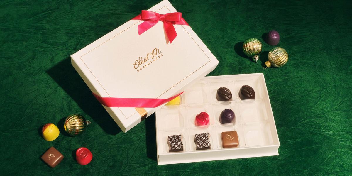 12 piece Cream CCB box with red ribbon on green background with various chocolate gems