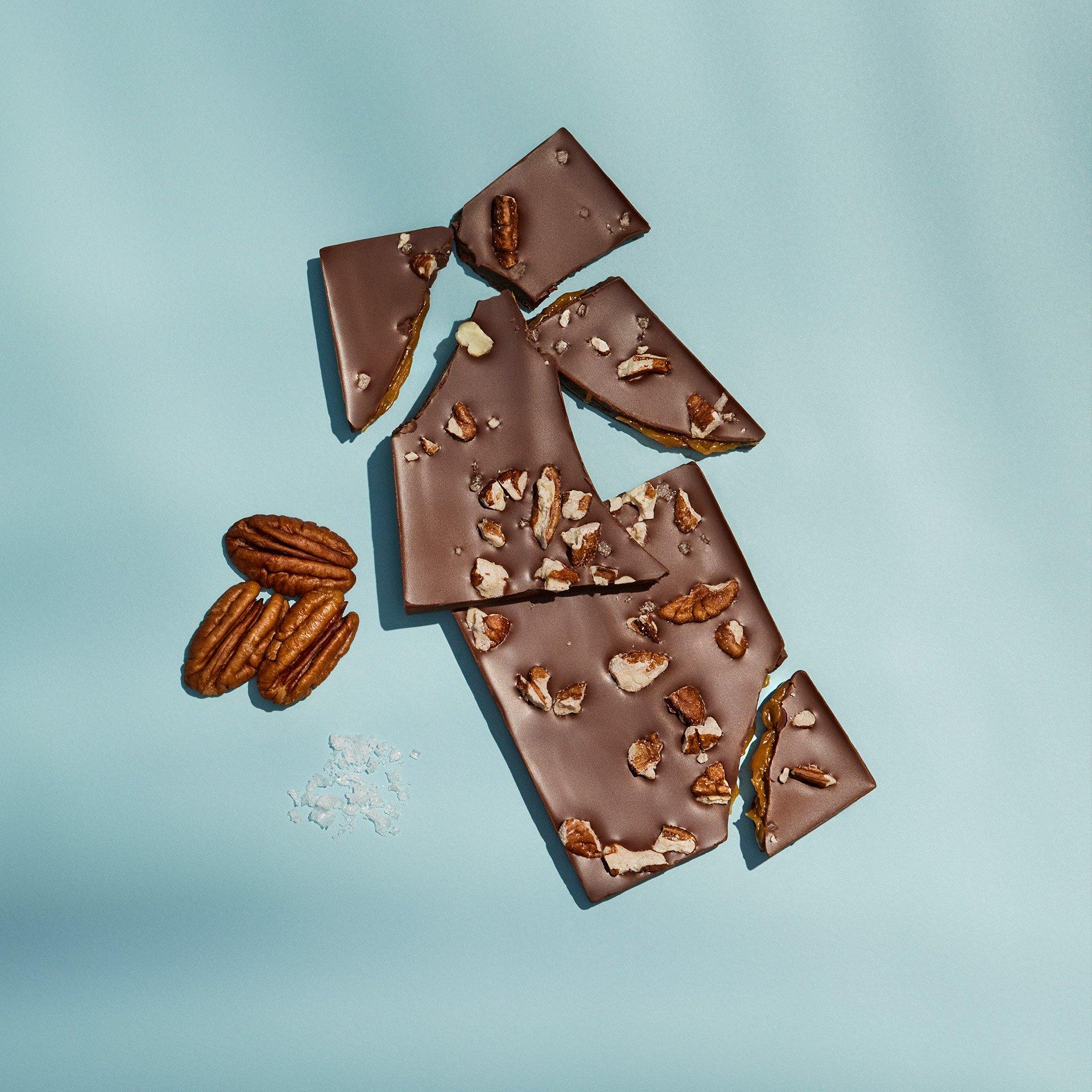 Ethel M Chocolates Pecan Caramel Rapture Table Bar broken into pieces with whole pecans next to the pieces.