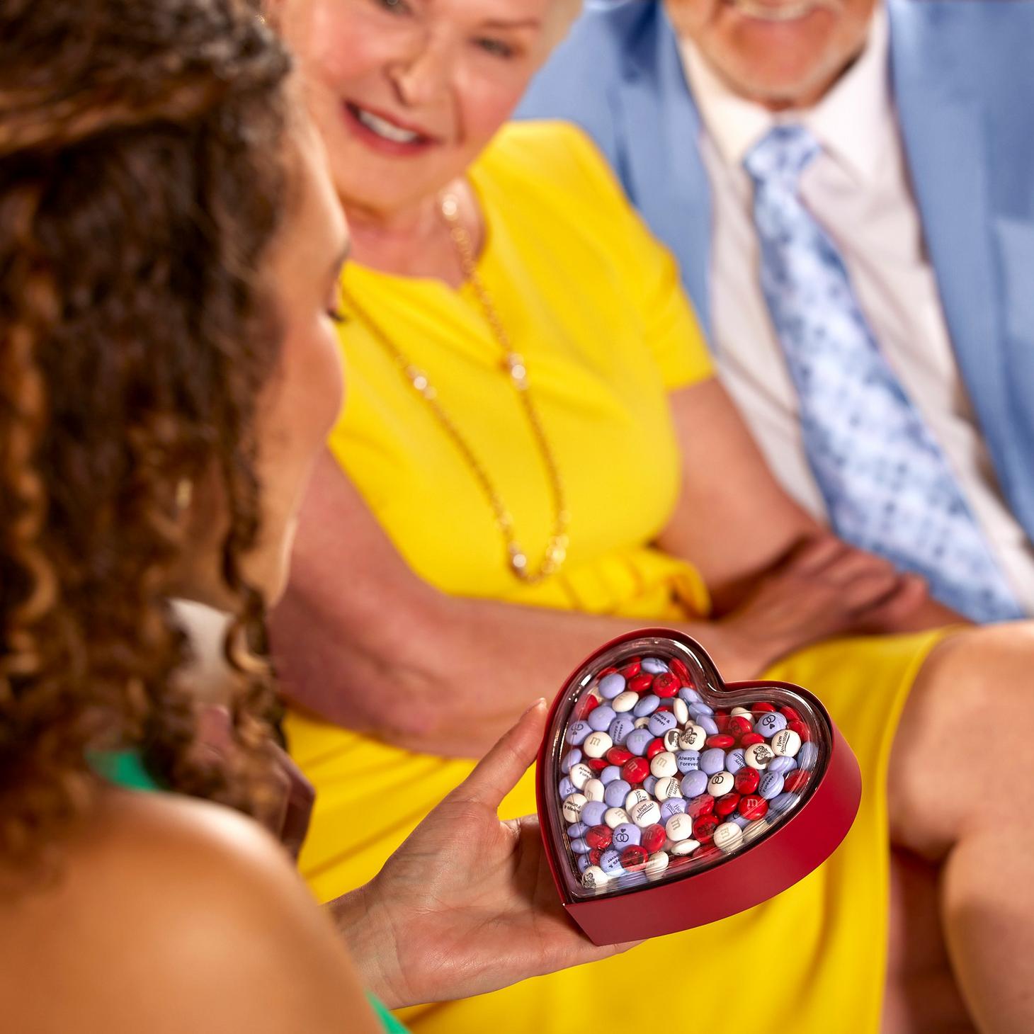 woman admiring heart gift box filled with M&M'S with grandparents in the background