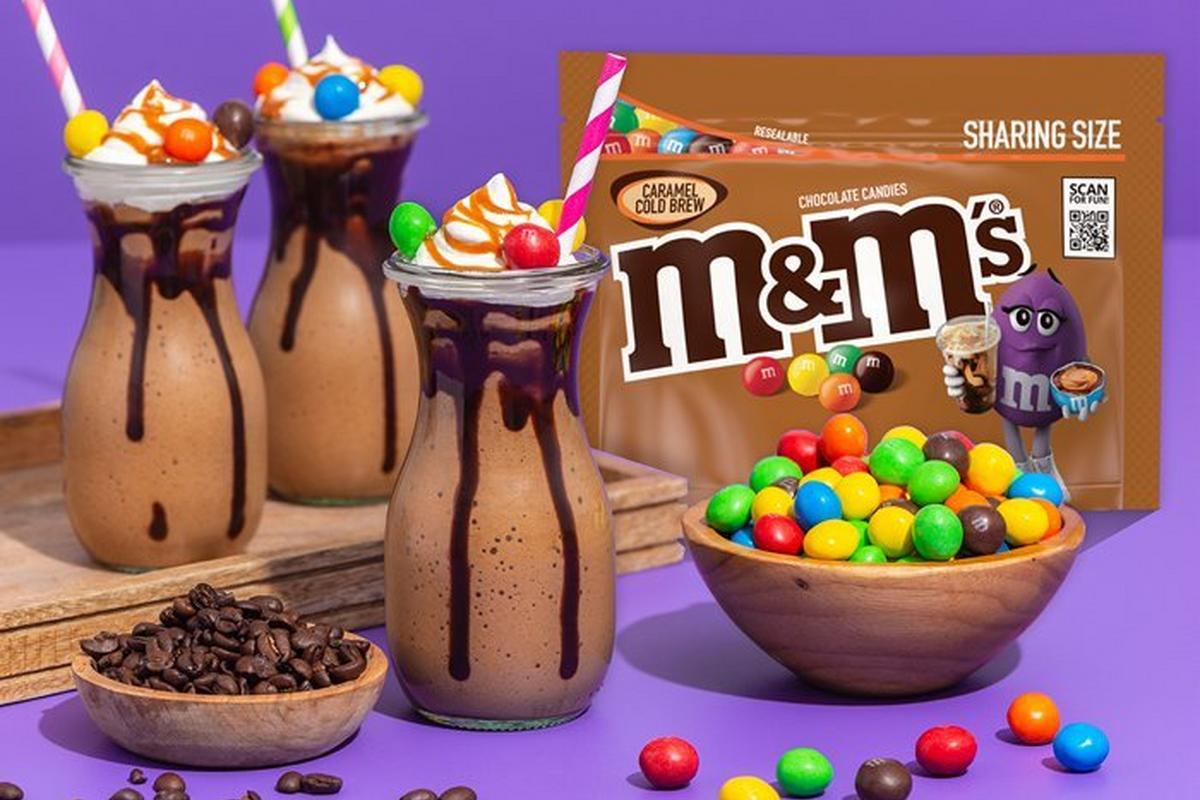 Three frappes with bowl of caramel cold brew M&M'S, a bowl of coffee beans and a bag of caramel cold brew M&M'S.