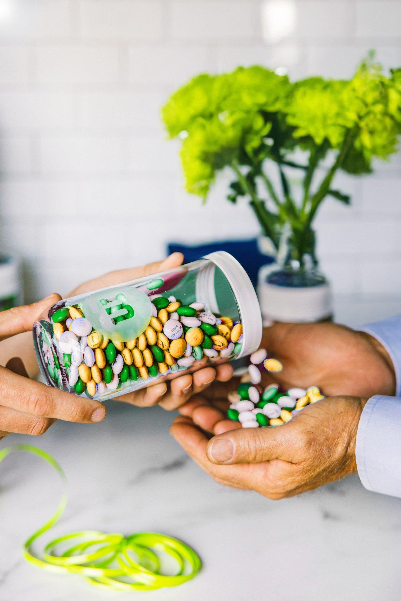 gift jar filled with St. Patrick's Day themed M&M'S being poured into another person's hand