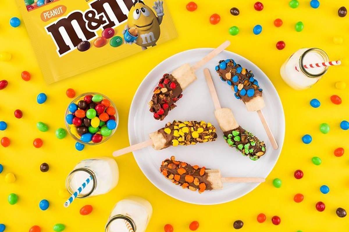 Frozen banana pops on a plate surrounded by glasses of milk.
