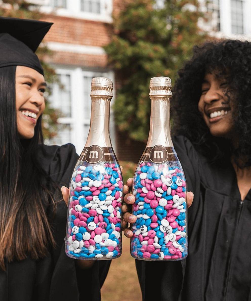two graduates holding up gift bottles