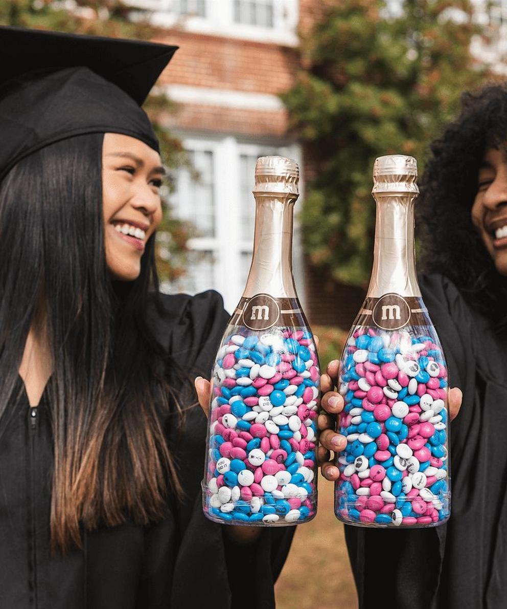 two graduates celebrating their success with M&M'S filled celebration bottles