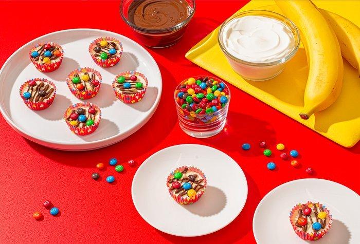 yogurt cups on plate with bowl of M&M'S and cutting board of banana