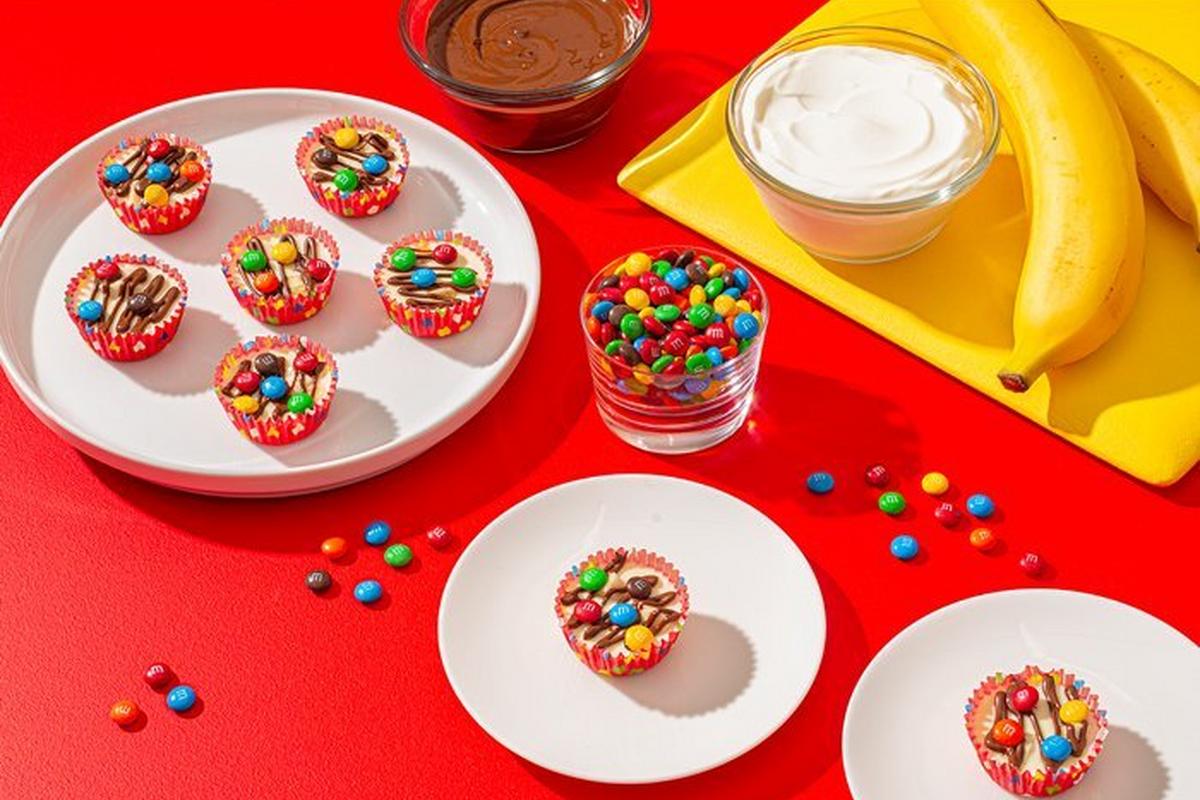 yogurt cups on plate with bowl of M&M'S and cutting board of banana