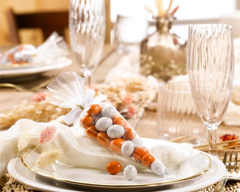 detalles de fiesta M&M'S Peanut blancos y naranjas en un servicio de mesa