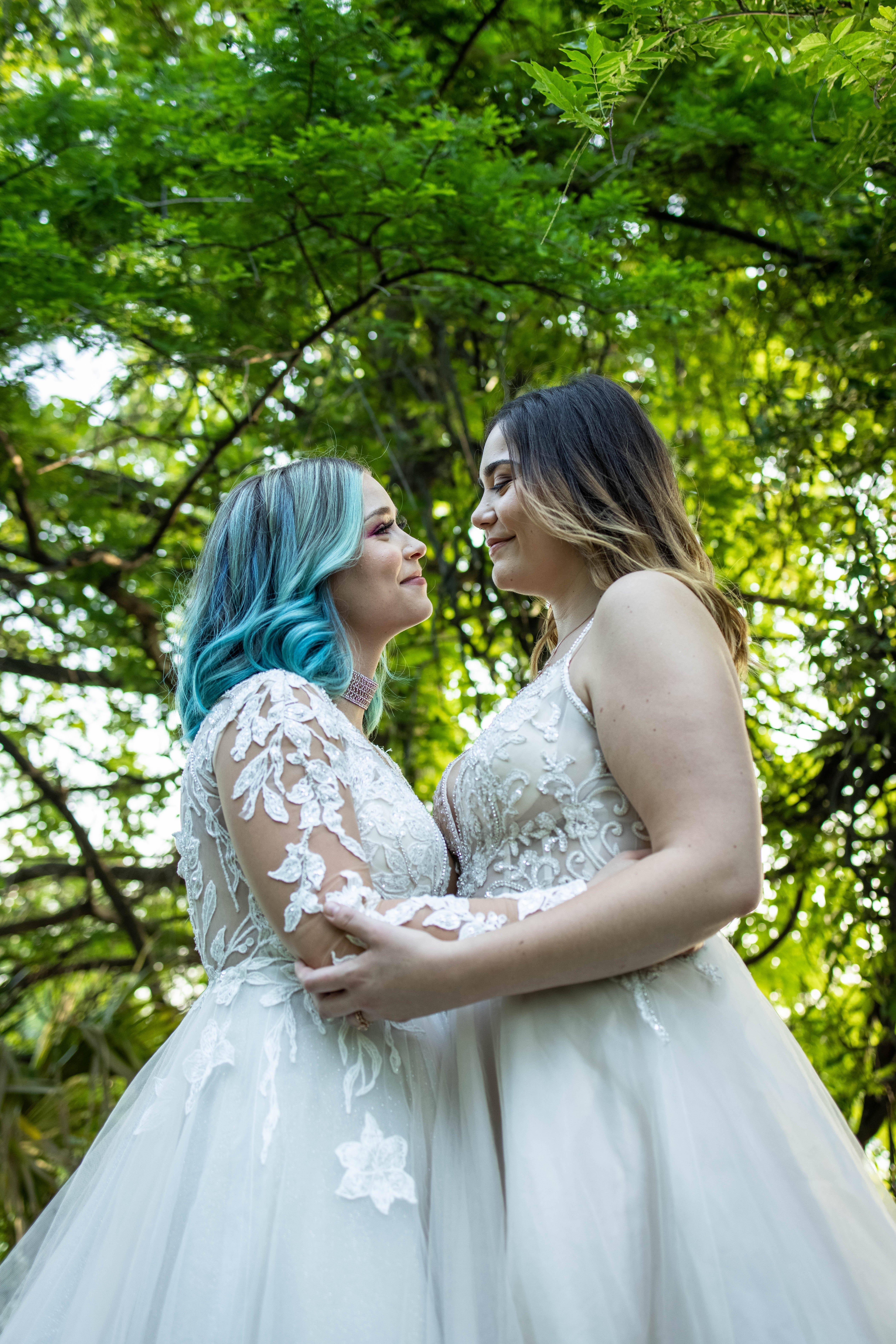 Two brides holding hands looking over a lake