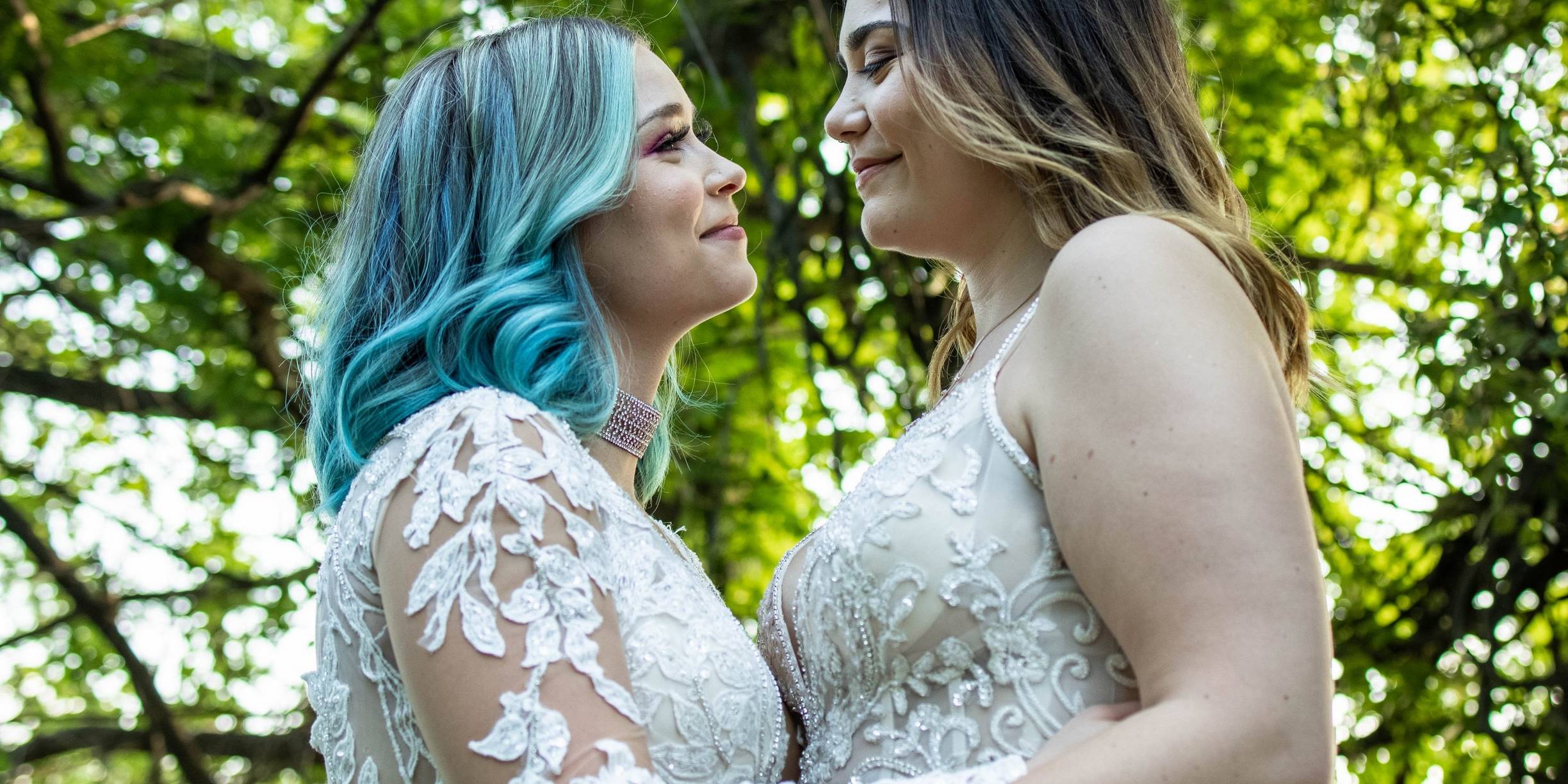 Two brides holding hands looking over a lake