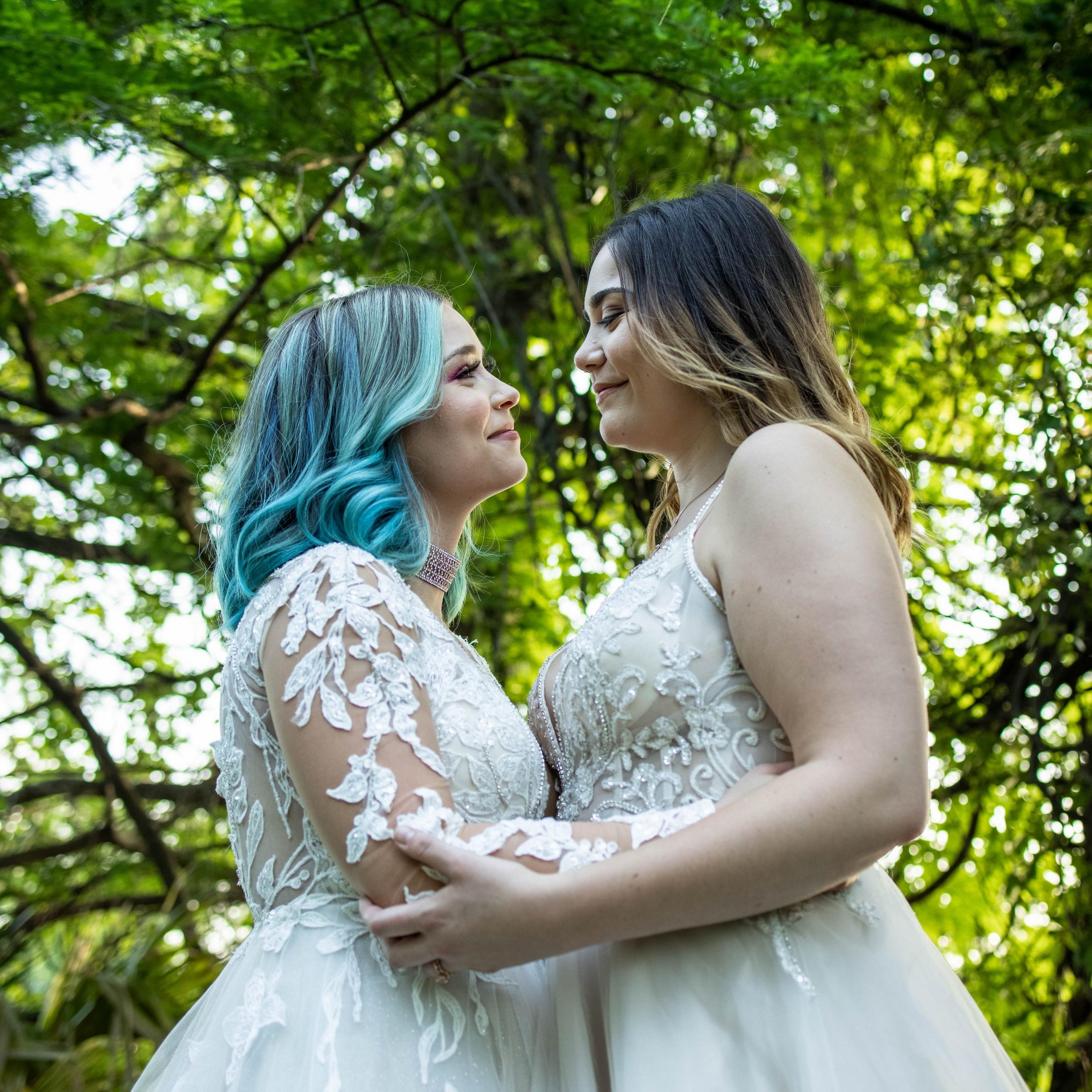 Two brides holding hands looking over a lake