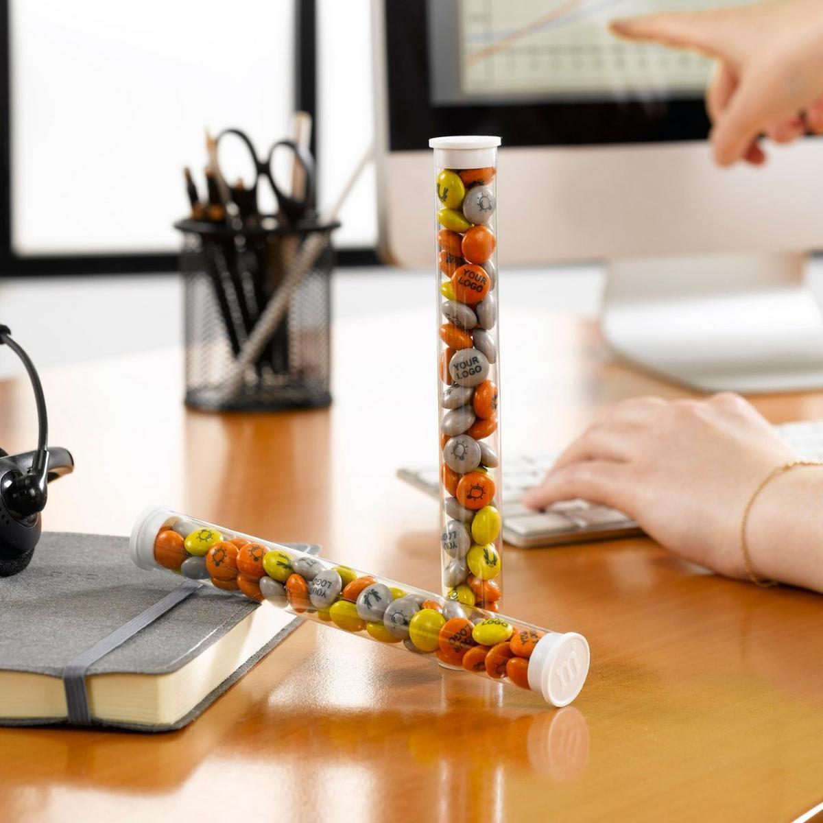 Two favor tubes filled with M&M'S on a desk as someone works at a computer.