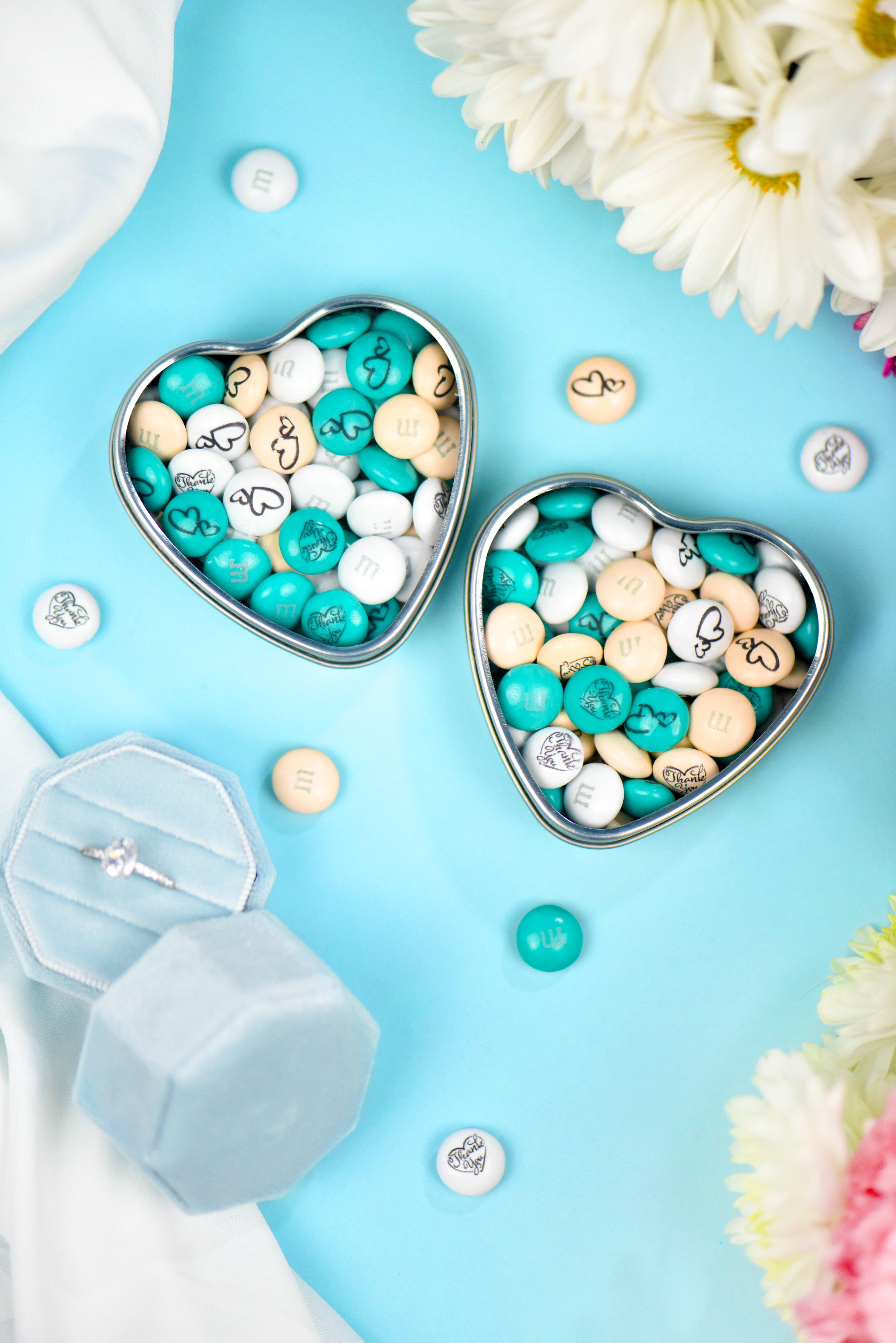 heart favor tins showing personalized M&M'S surrounded by wedding props
