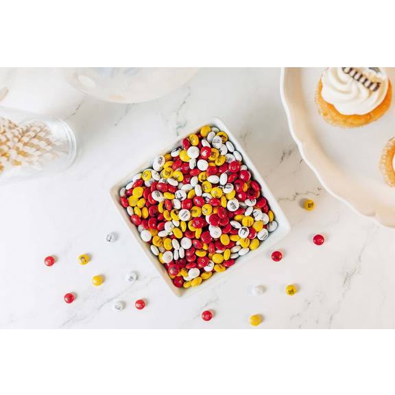 White square bowl filled with M&M'S candies in red, yellow, and white on a marble surface.