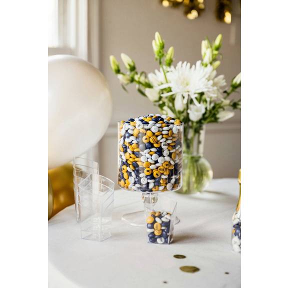 Clear dispenser filled with M&M'S chocolate candies in gold, white, and navy blue with 2023 printed on some candies.