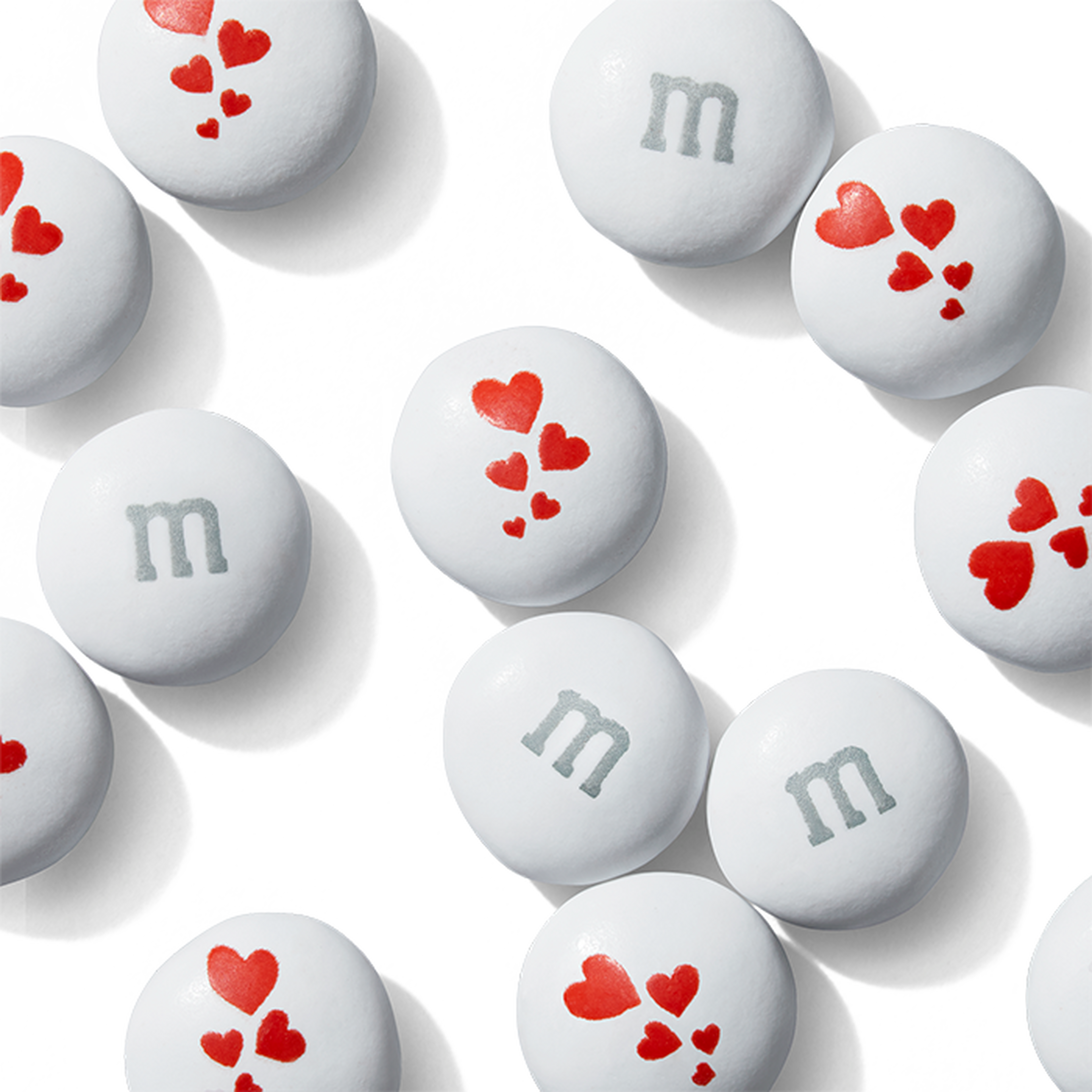 White M&M'S candies with gray lowercase m and red heart designs printed on the shells.