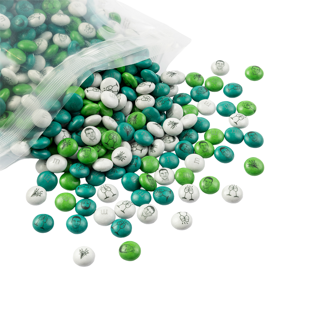 M&M'S Schokolinsen in Grün-, Weiß- und Türkistönen, die aus einem transparenten Beutel verschüttet sind, mit aufgedruckten Feiertagsmotiven.