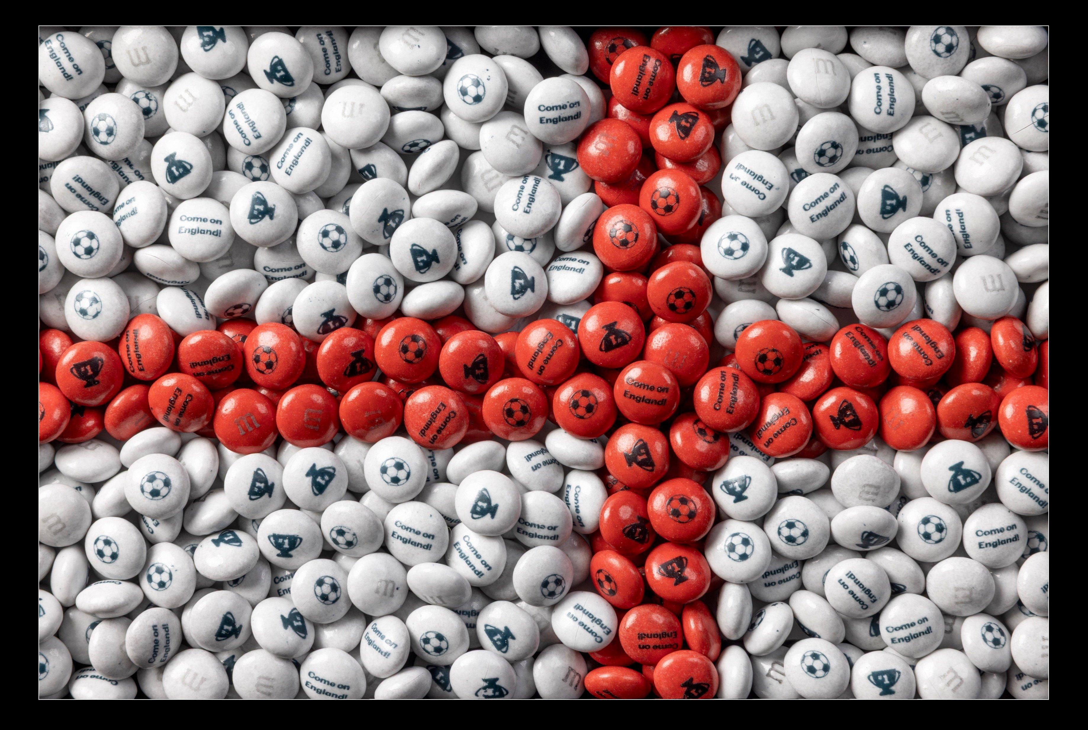 Dulces de M&M'S blancos y rojos formando la bandera de Inglaterra, con balones de fútbol, trofeos y el texto "Come on England!" impresos.